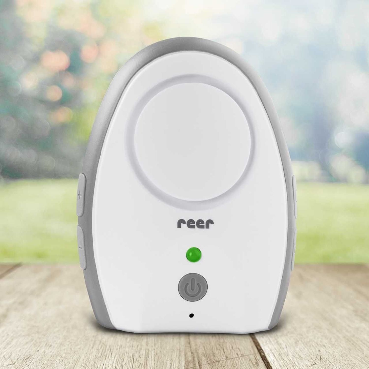 Ein weißes Babyfon mit grauem Rand steht auf einem Holztisch im Freien.
