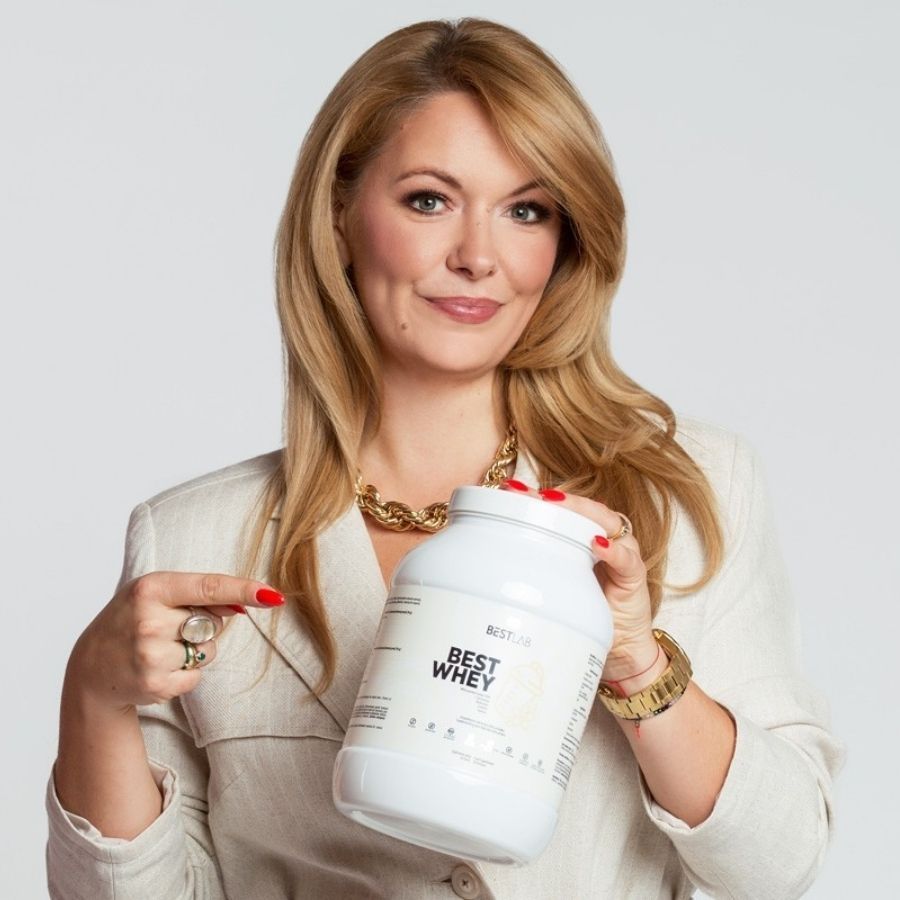 Frau hält ein weißes Best Lab Whey Proteinpräparat. Logo und Schriftzug "BEST WHEY" auf der Vorderseite. Sie zeigt darauf.