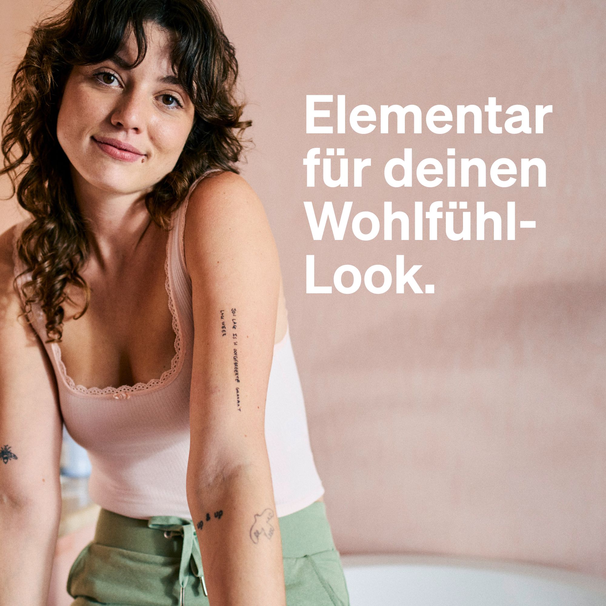 Frau mit Tattoo und Armband. Text: Elementar für dein Wohlfühl-Look. Rosa Wand im Hintergrund.