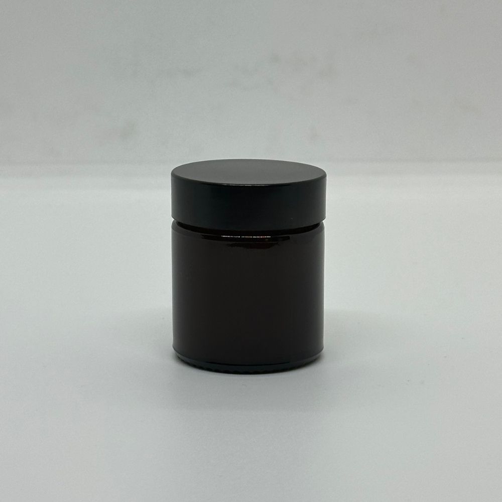 Braune Glasdose mit schwarzem Deckel. Zylindrische Form, auf hellem Hintergrund.