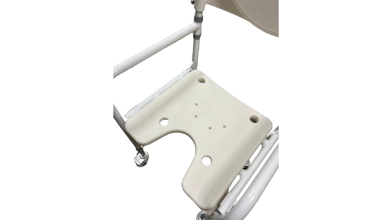 Nahaufnahme der Sitzfläche eines Duschstuhls mit Rädern. Beige, mit Aussparung und Löchern. Weißes Gestell und Armlehnen.