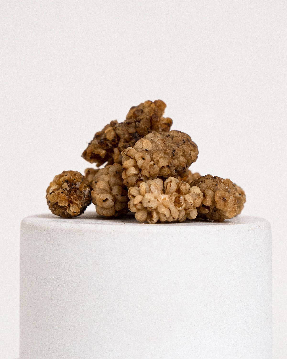 Haufen getrockneter, weißer Maulbeeren auf einem weißen Podest. Die Beeren sind unregelmäßig geformt und haben eine bräunliche Farbe.