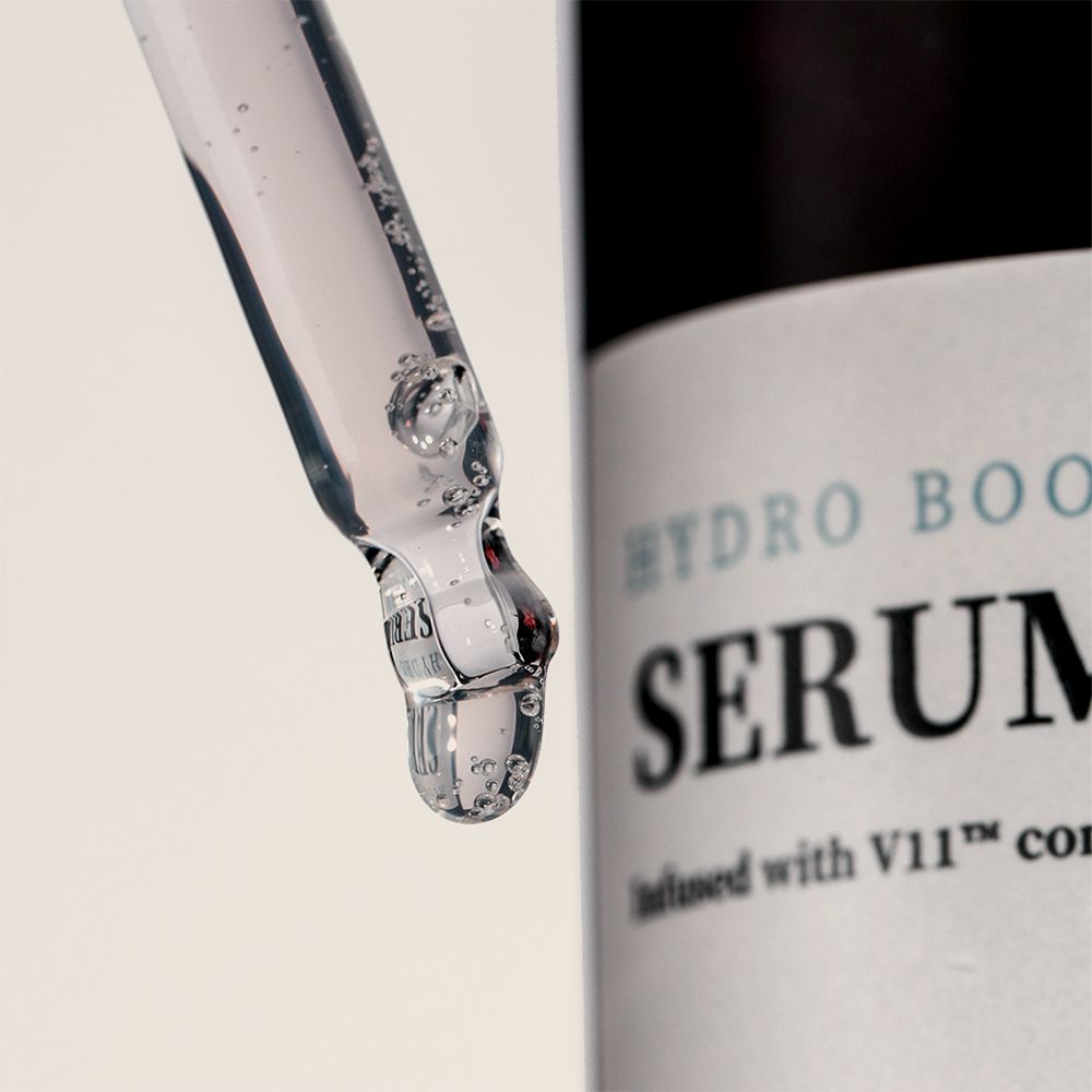 Nahaufnahme einer Pipette mit Serum. Serum ist klar und enthält Bläschen. Flasche im Hintergrund mit Text: HYDRO BOOST SERUM.