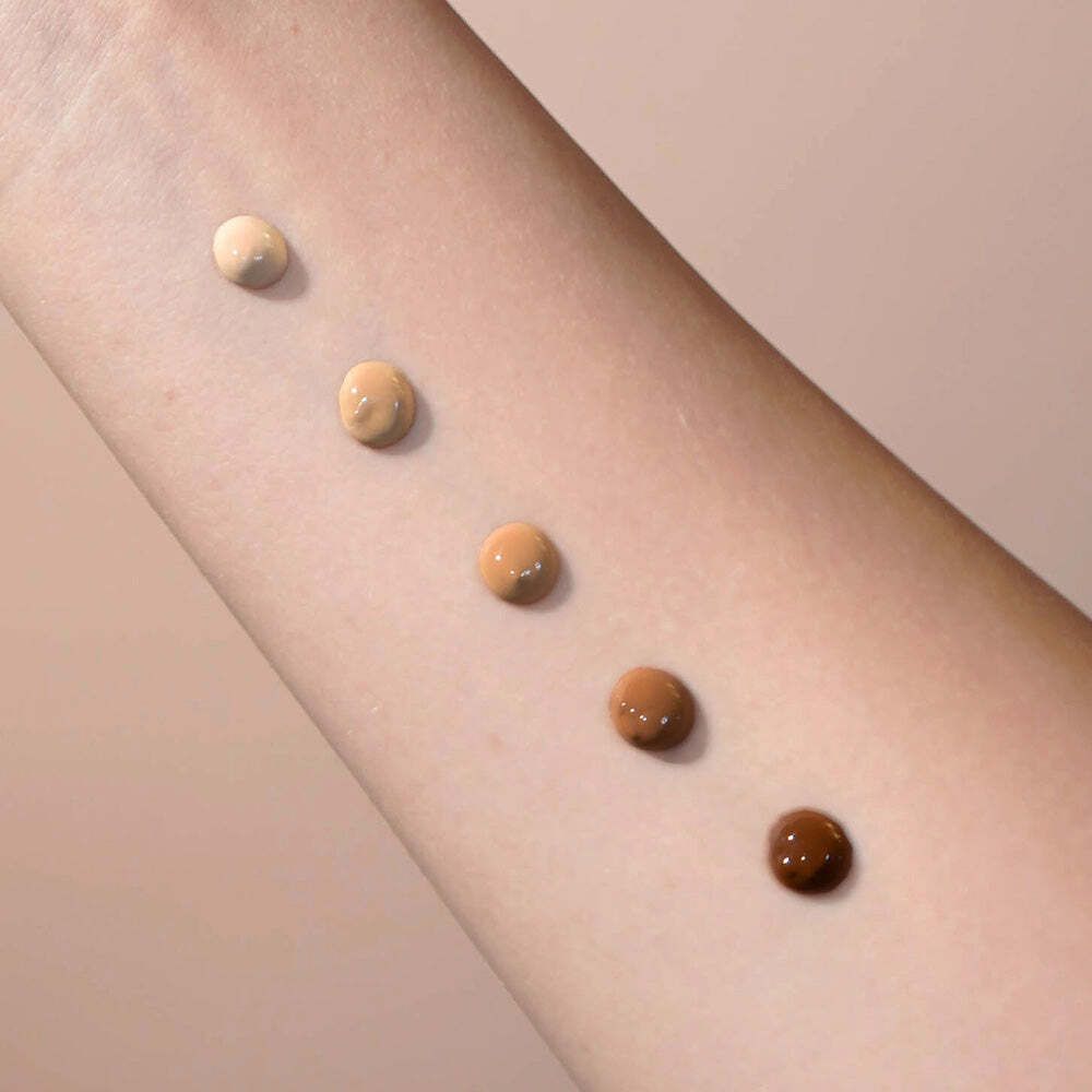 Arm mit fünf Farbtupfern des getönten Serums. Von hell nach dunkel: Beige, hellbraun, mittelbraun, dunkelbraun, sehr dunkelbraun.