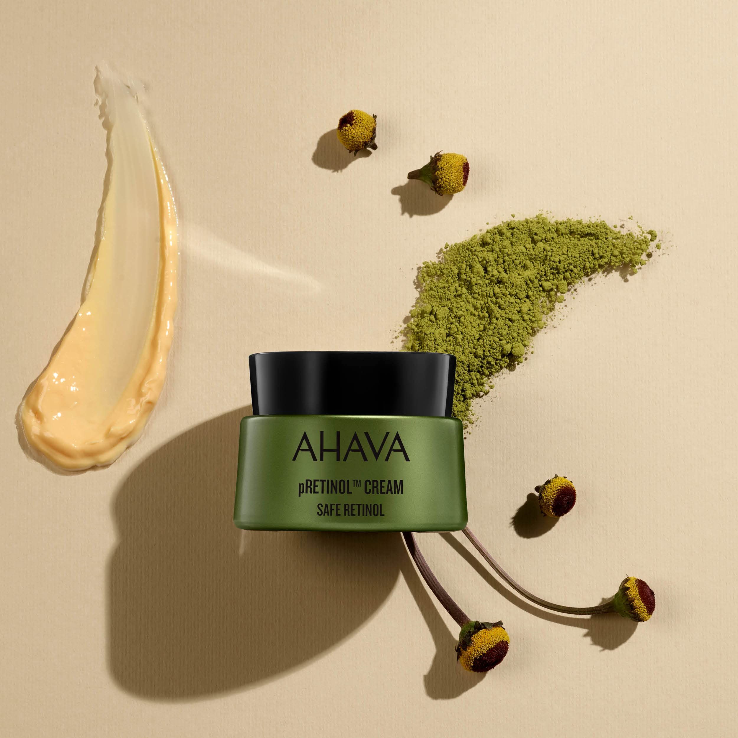 Grüne Creme-Dose mit schwarzem Deckel, daneben Creme-Spur, Kräuter und Blüten.