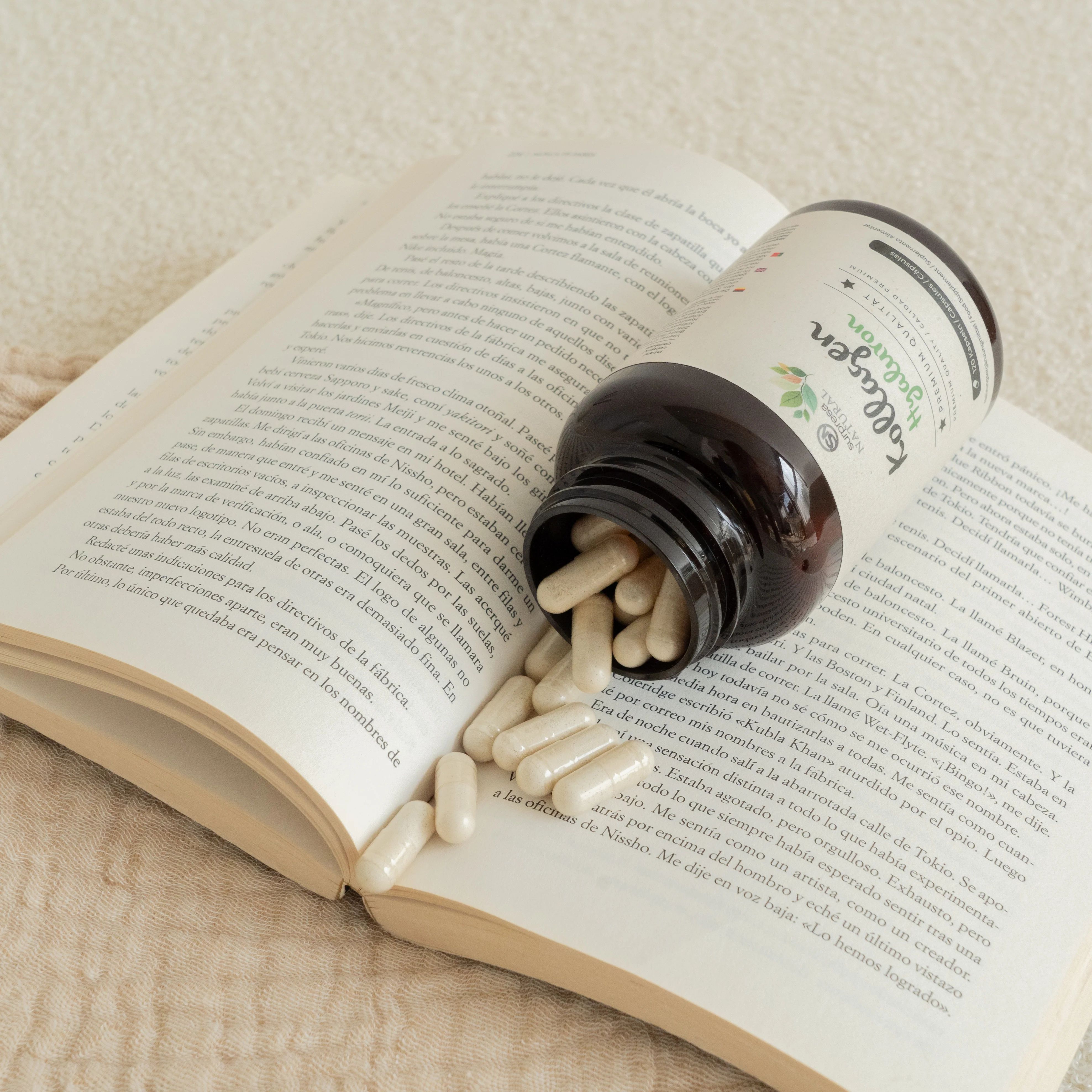 Braune Flasche mit Kapseln liegt auf einem offenen Buch. Kapseln sind verstreut. Aufschrift: Surpresa Natural, Kollagen Hyaluron.