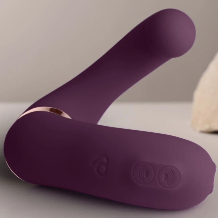 Lila Vibrator mit gebogener Form. Goldfarbener Akzent. Auf hellem Untergrund.