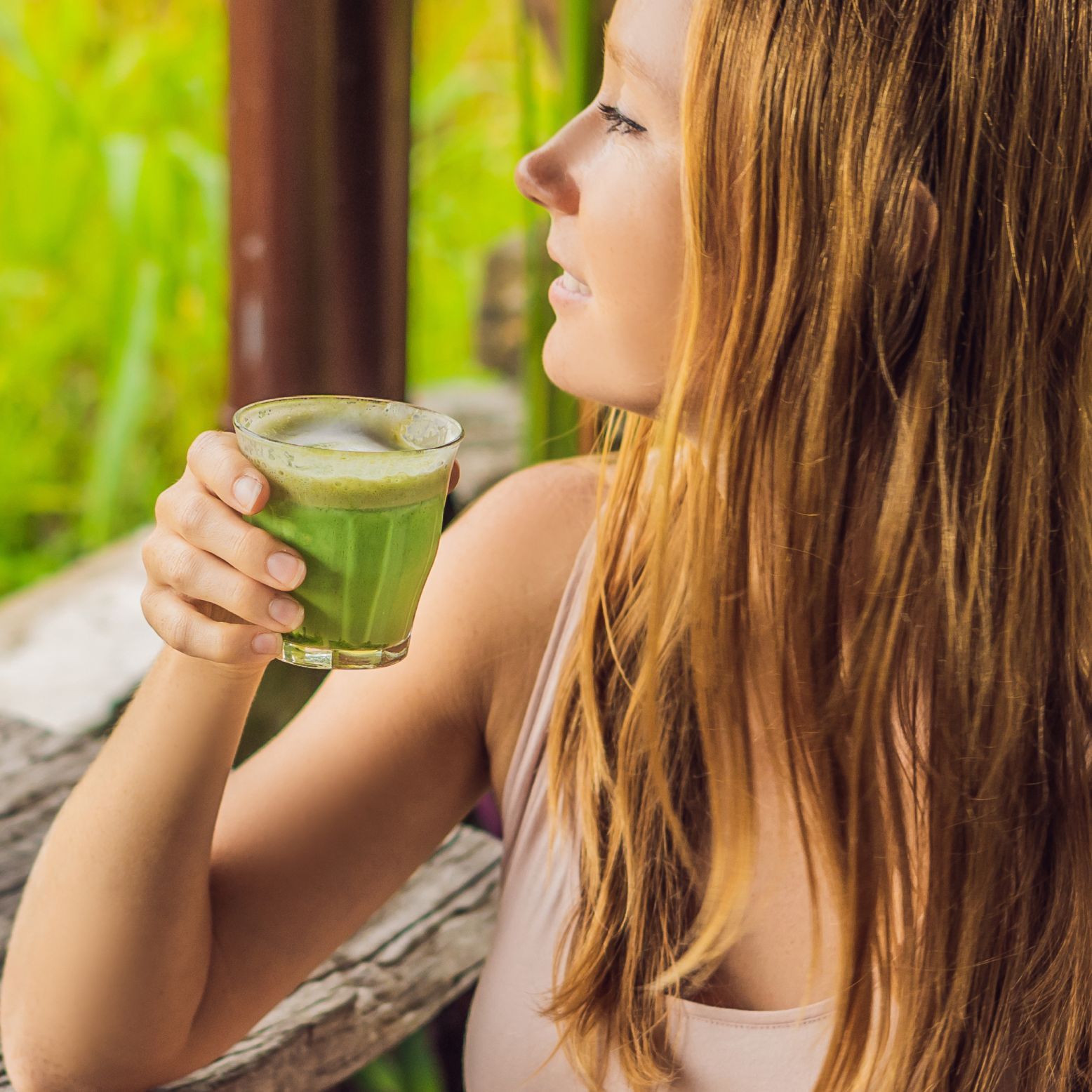 Eine Frau hält ein Glas Matcha-Tee. Der Tee ist grün und in einem Glasbecher. Die Frau ist im Profil zu sehen.