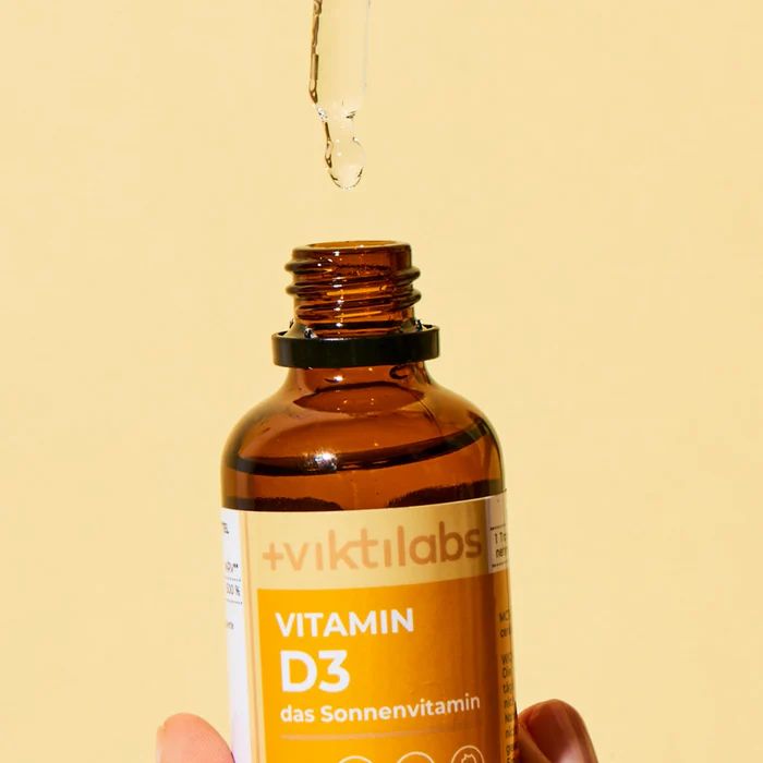Braune Glasflasche mit schwarzem Deckel. Tropfen aus der Pipette. Gelbes Etikett mit Text: Vitamin D3, das Sonnenvitamin. Viktilabs Logo.