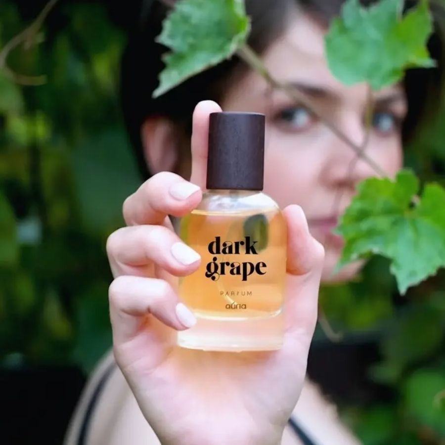 Parfumflasche mit braunem Deckel, gehalten von einer Hand. Aufschrift "dark grape parfum" und "auna".