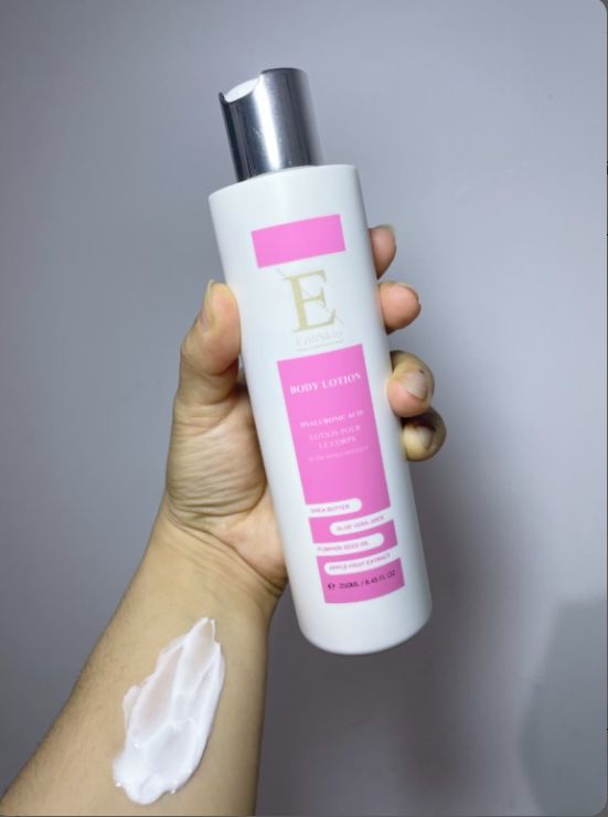 Weiße Flasche mit rosa Etikett. Silberne Kappe. Hand hält Flasche und Creme auf Arm. Text: Body Lotion, Hyaluronsäure + Kollagen, Aloe Vera, Granatapfel.