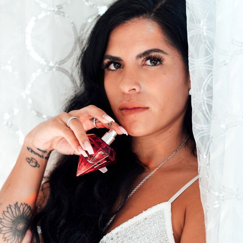 Frau hält einen roten Diamant-Parfümflakon. Sie trägt ein weißes Oberteil und hat lange, dunkle Haare.