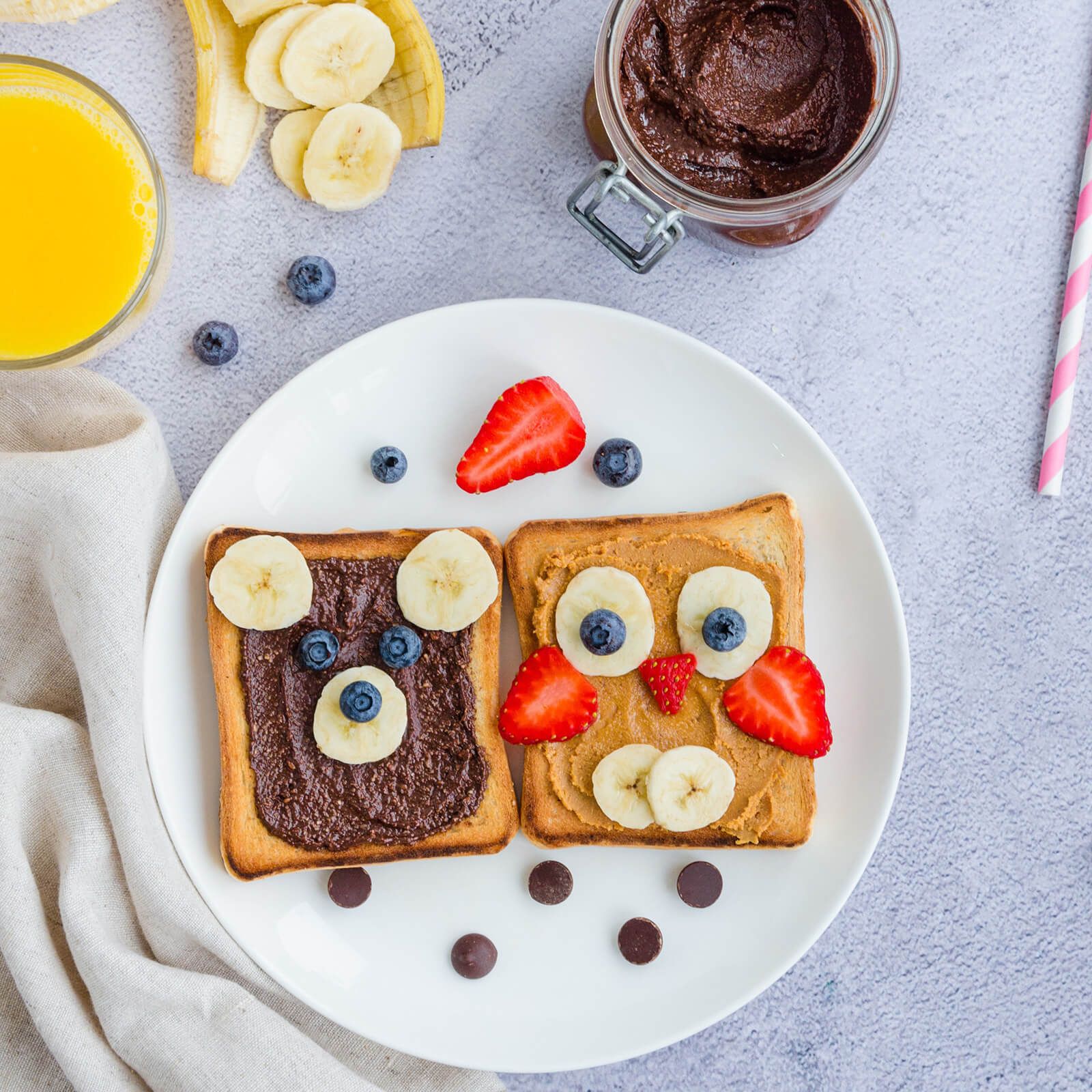 Zwei Toastscheiben, dekoriert als Bär und Eule mit Nussbutter, Früchten und Beeren.