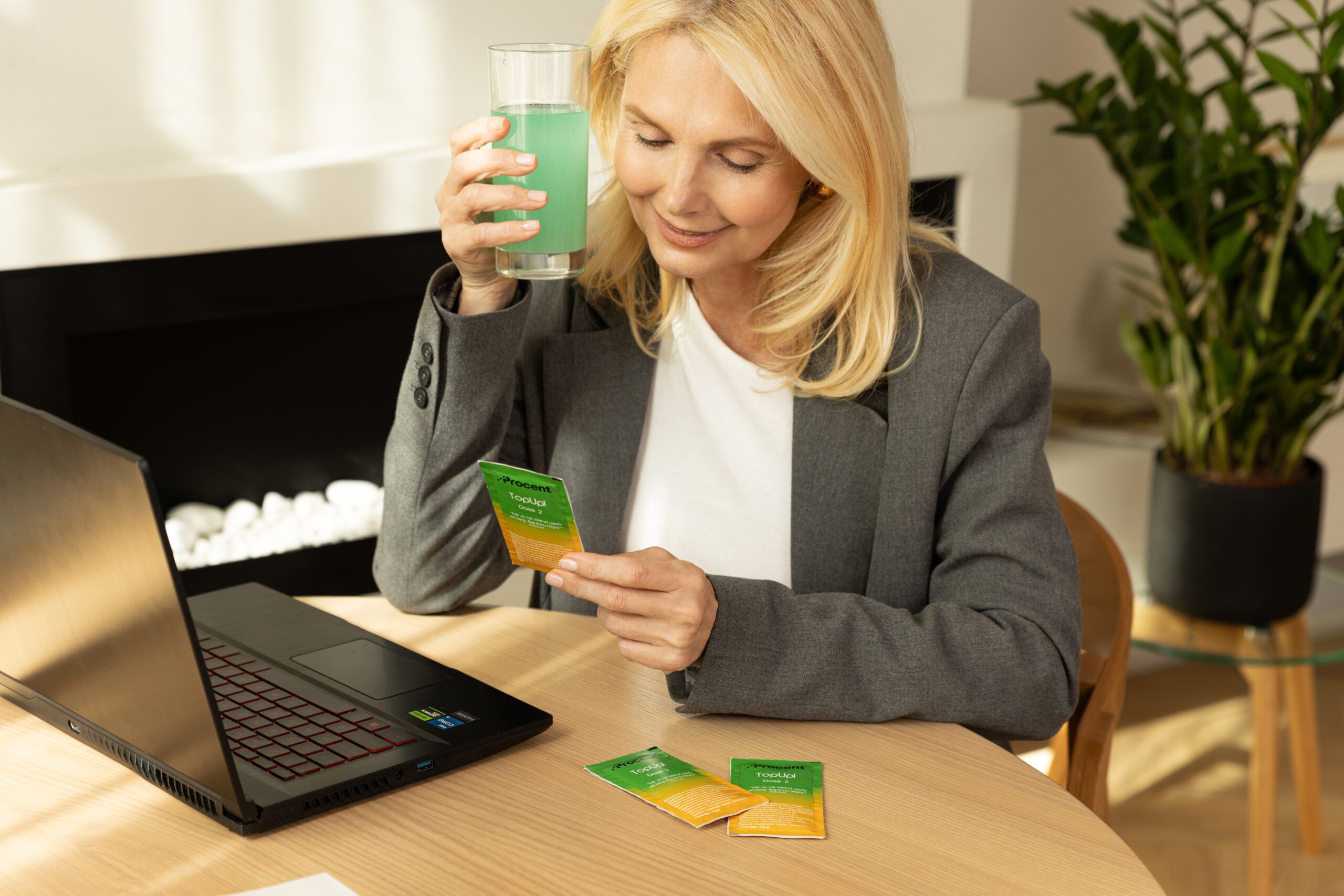 Frau mit Getränk und PROCENT-Beutel. Auf dem Tisch: Laptop, zwei weitere Beutel.