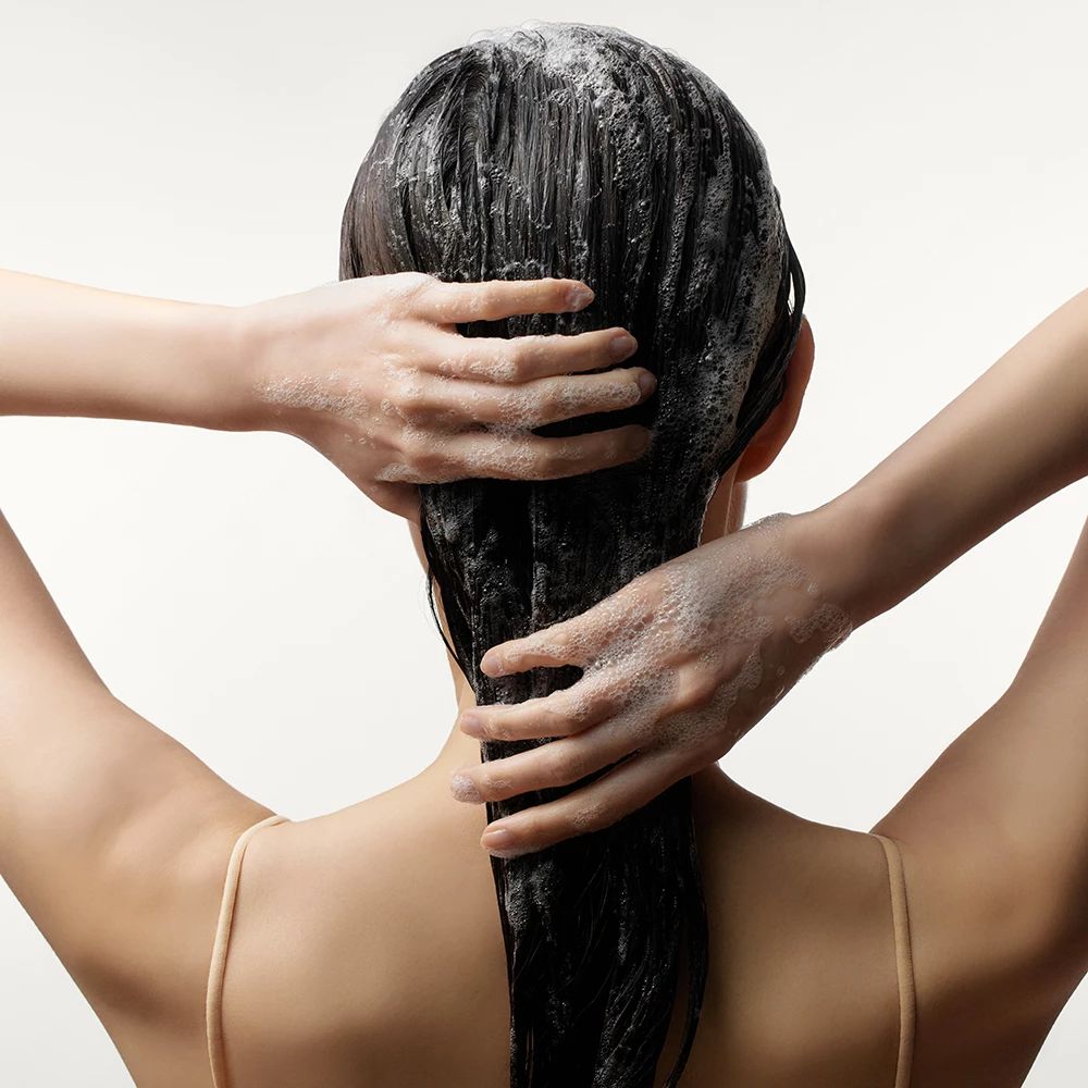 Person wäscht Haare mit Schaum. Hände am Hinterkopf. Blick von hinten.