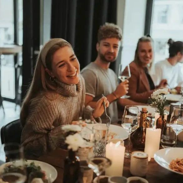 Mehrere Personen sitzen an einem Tisch. Essen und Getränke sind vorhanden. Kerzen und Dekorationen.