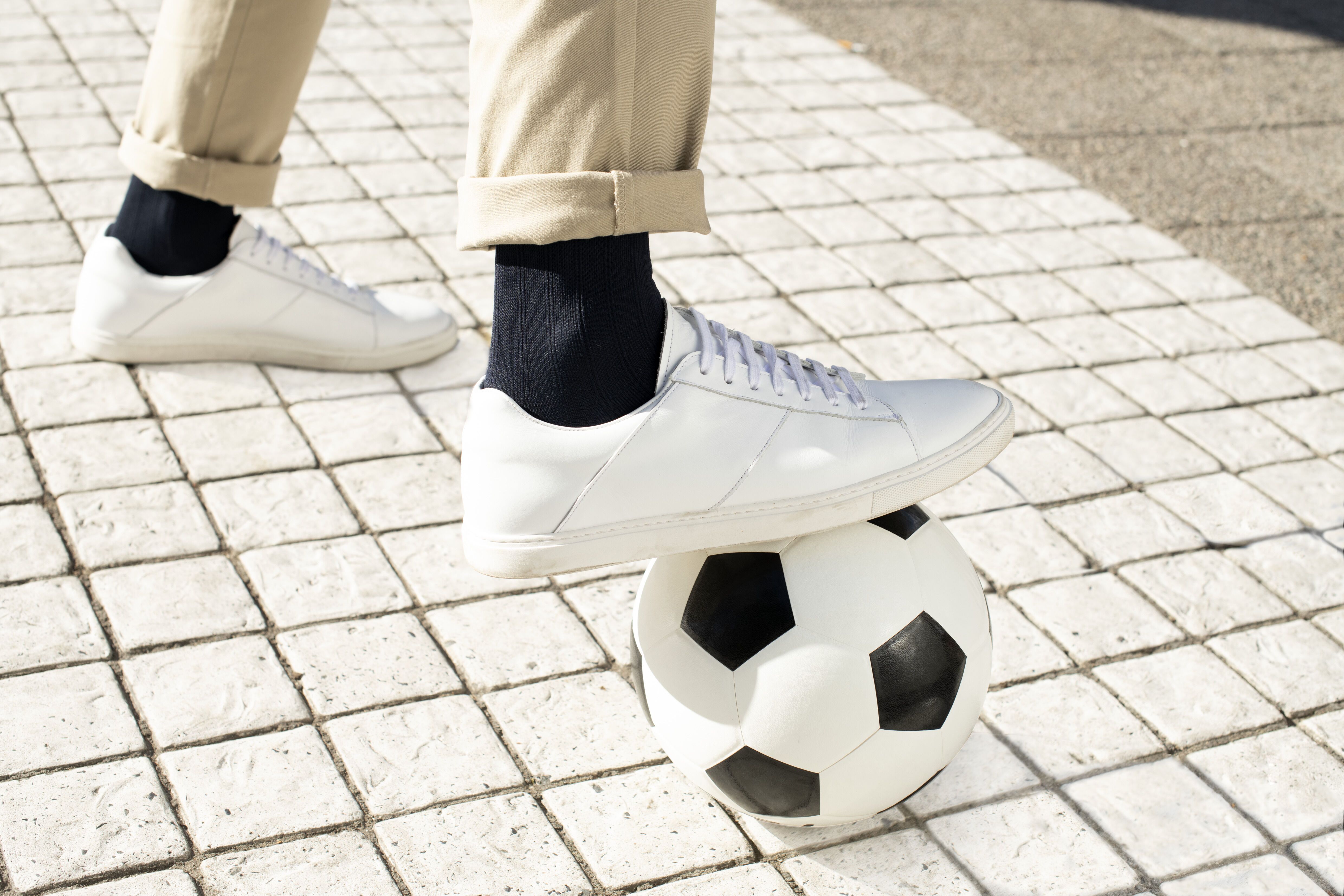Man met witte schoenen en zwarte compressiekousen. Staat op een voetbal.