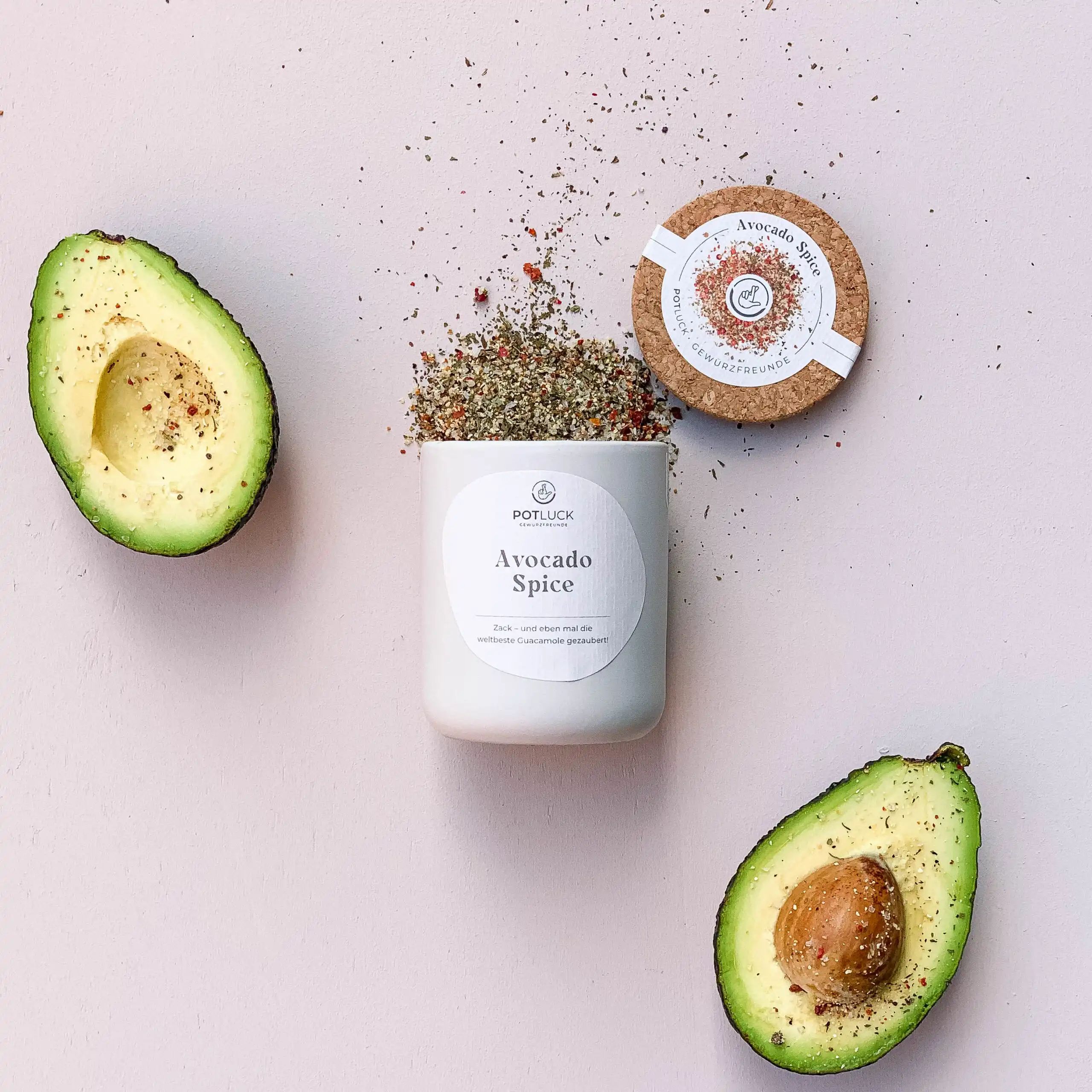Keramikgefäß mit "POTLUCK Avocado Spice", daneben Avocadohälften und Korkdeckel mit Label.