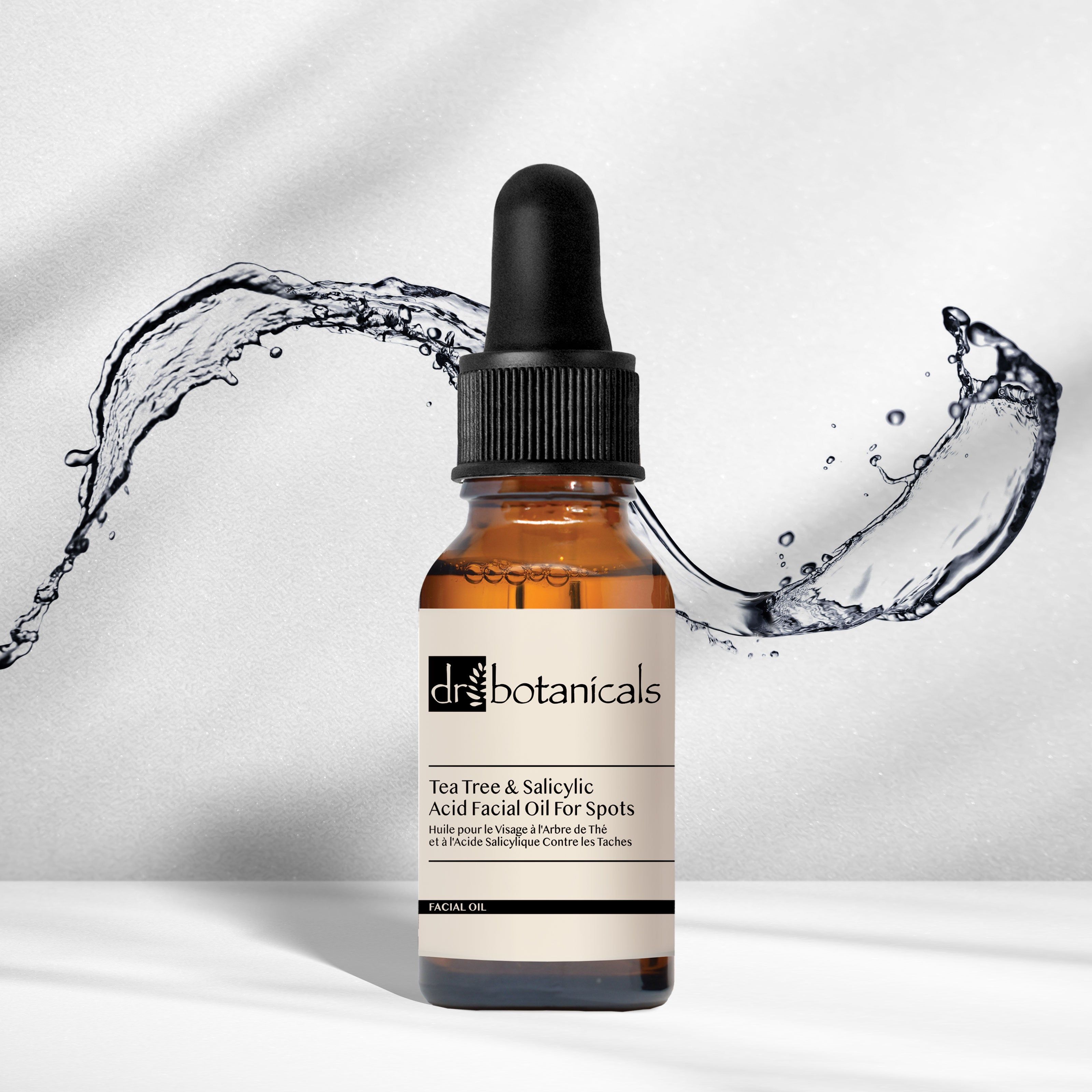 Braune Glasflasche mit schwarzem Tropfer. Aufschrift: Dr Botanicals, Tea Tree & Salicylsäure Gesichtsöl für Flecken. Wasserspritzer.