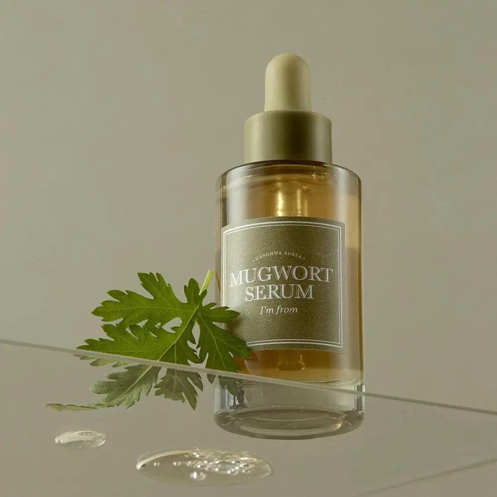 Glasflasche mit Serum, grüner Aufschrift "Mugwort Serum". Grüne Blätter daneben. Tropfen auf Glasoberfläche.