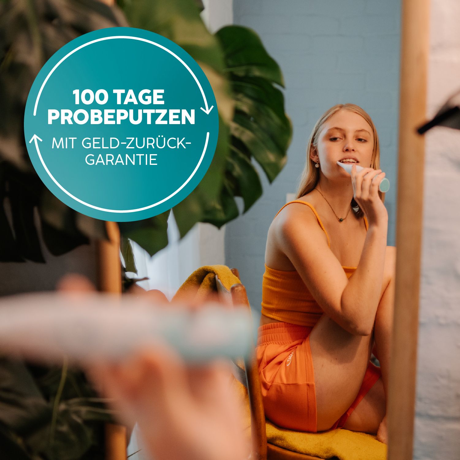 Frau putzt sich die Zähne vor dem Spiegel mit einer hellblauen Schallzahnbürste. Text: '100 Tage Probeputzen'.