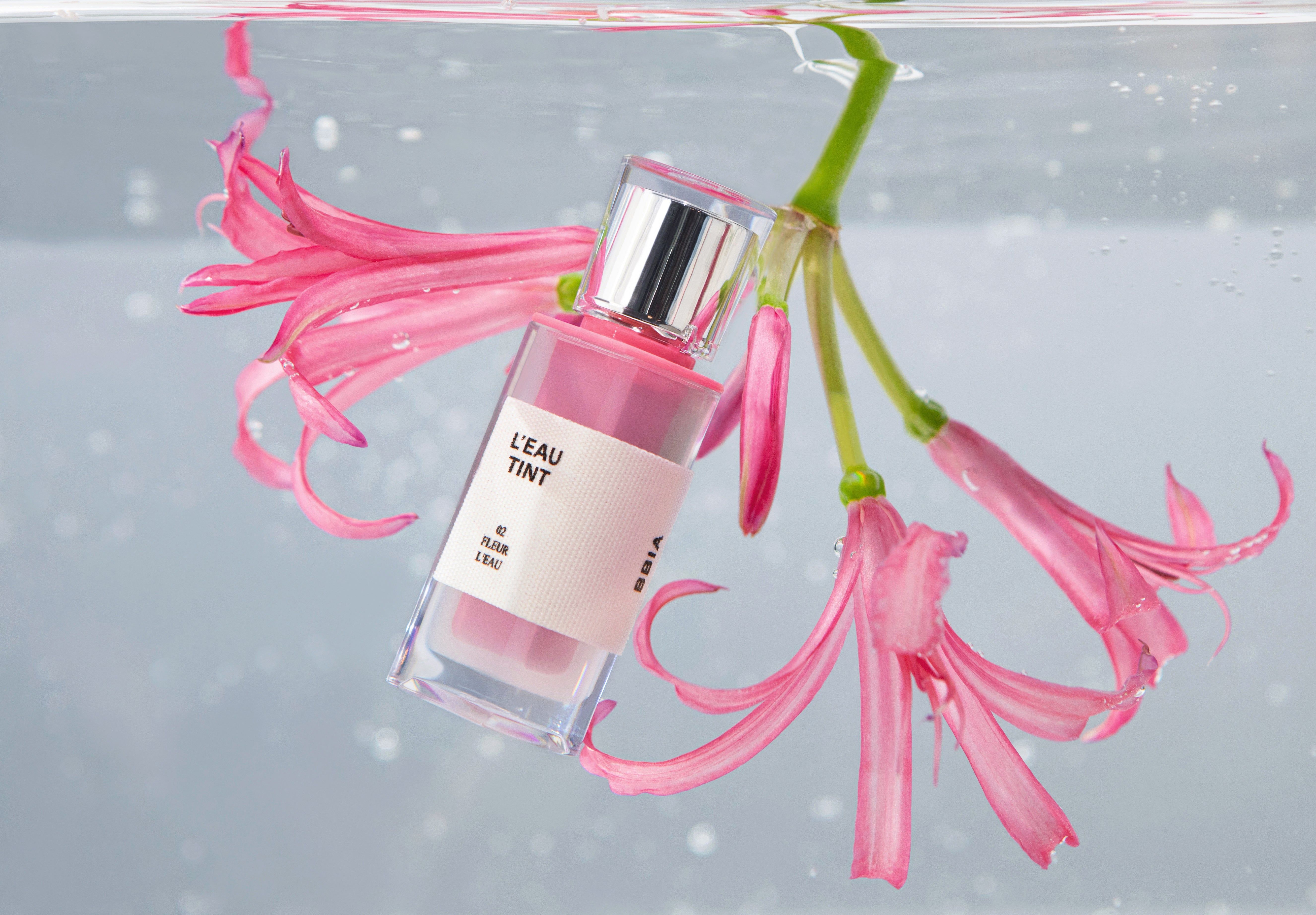 Lippenfarbflasche mit Blüten in Wasser. Rosa Blüten, transparente Flasche.