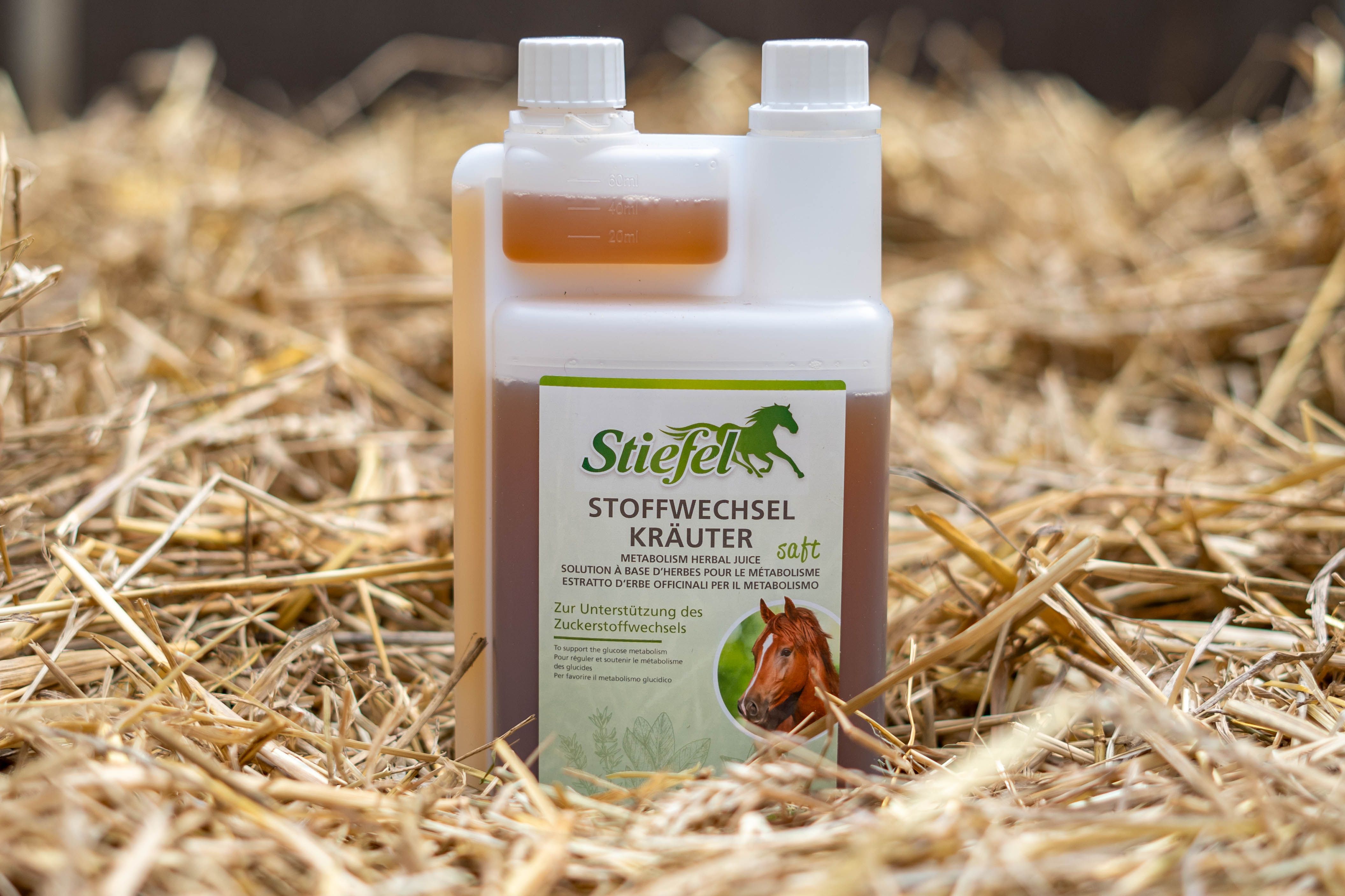 Flasche Stiefel Stoffwechselkräuter auf Stroh. Weißer Deckel, grünes Etikett mit Pferd. Text: Stoffwechselkräuter.