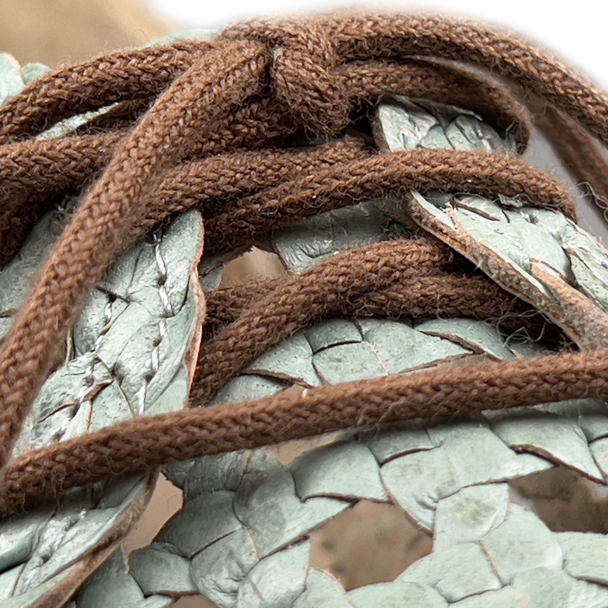 Nahaufnahme der braunen Schnürsenkel und des hellgrünen, gewebten Schuhmaterials. Lochmuster sichtbar.