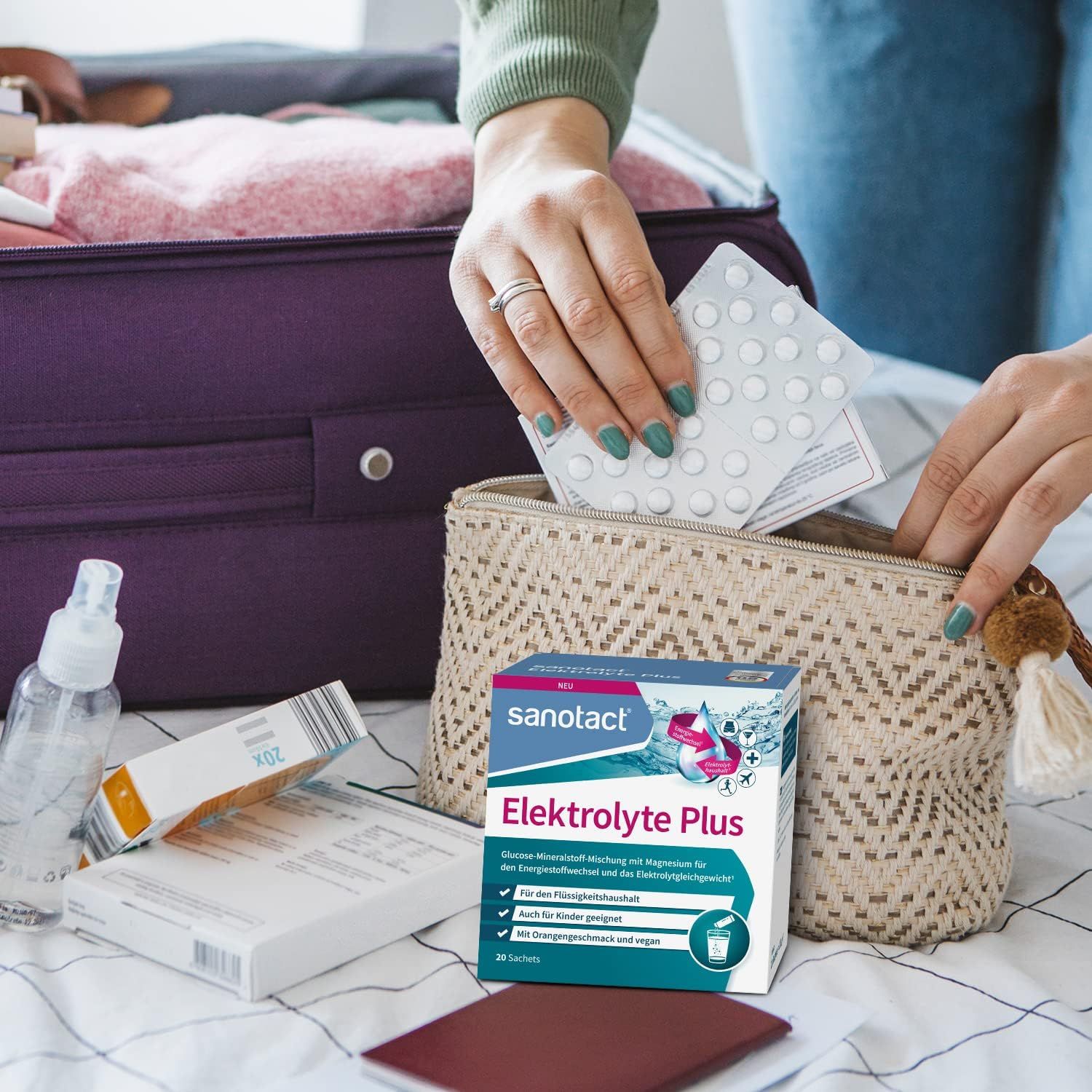 Person packt sanotact Elektrolyte Plus in eine Kosmetiktasche. Daneben liegen weitere Produkte und ein Koffer.