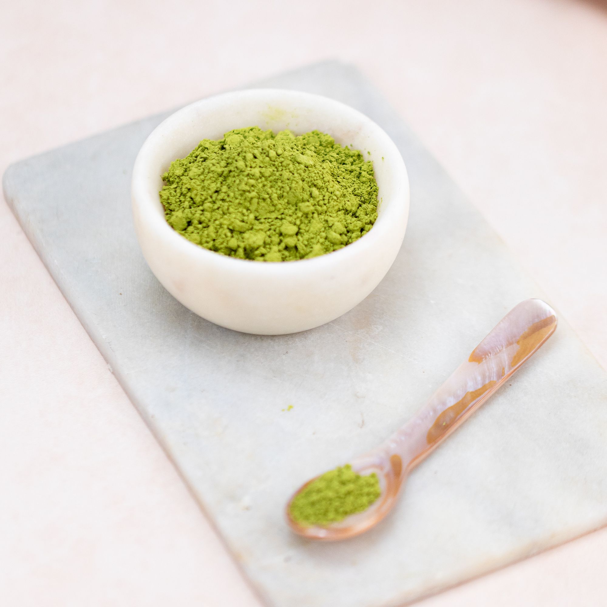 Schale mit Matcha-Pulver und Löffel. Auf Marmorplatte. Hintergrund unscharf.
