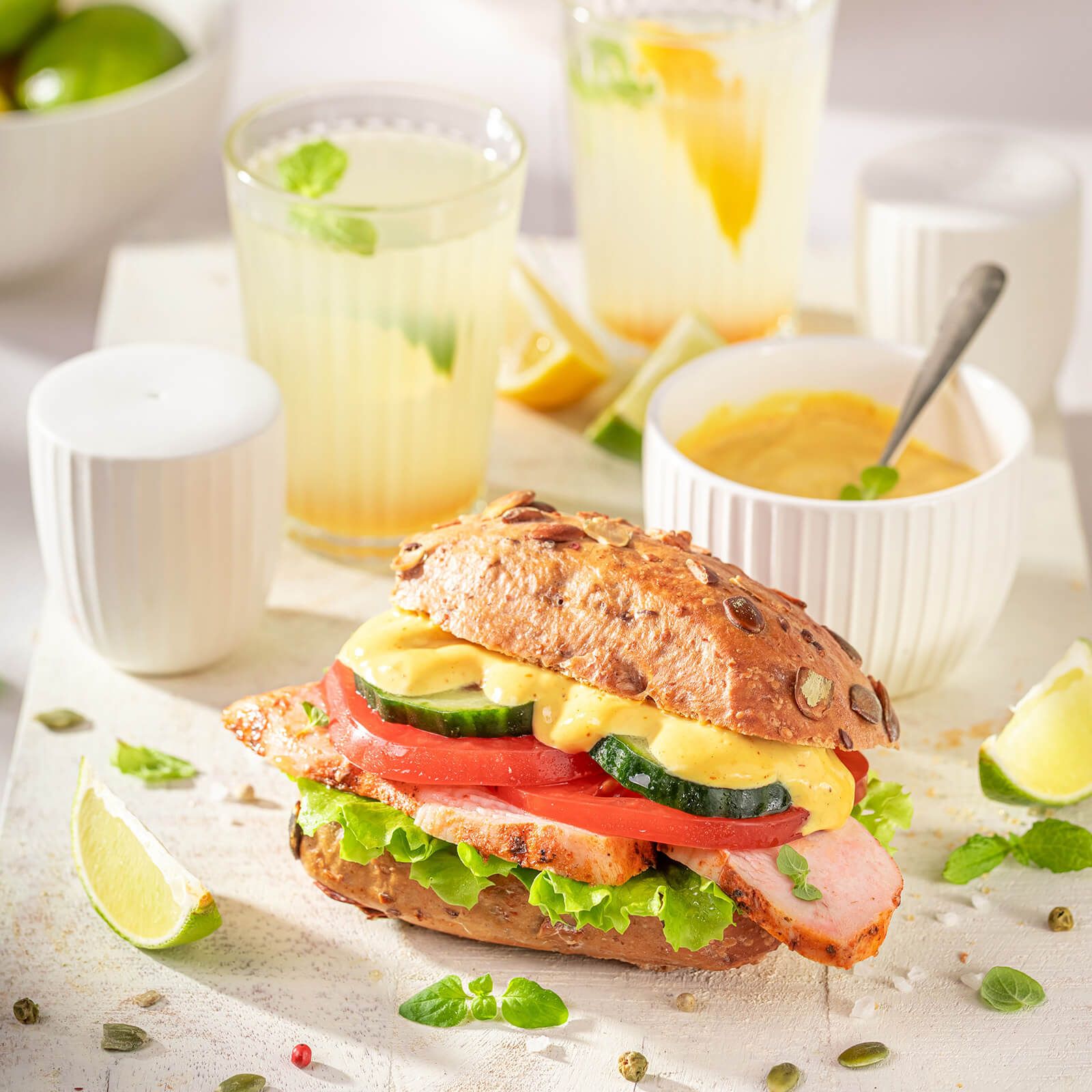 Sandwich mit Kürbis-Käse-Brötchen, Fleisch, Salat, Tomate, Gurke und Sauce, serviert mit Getränken.
