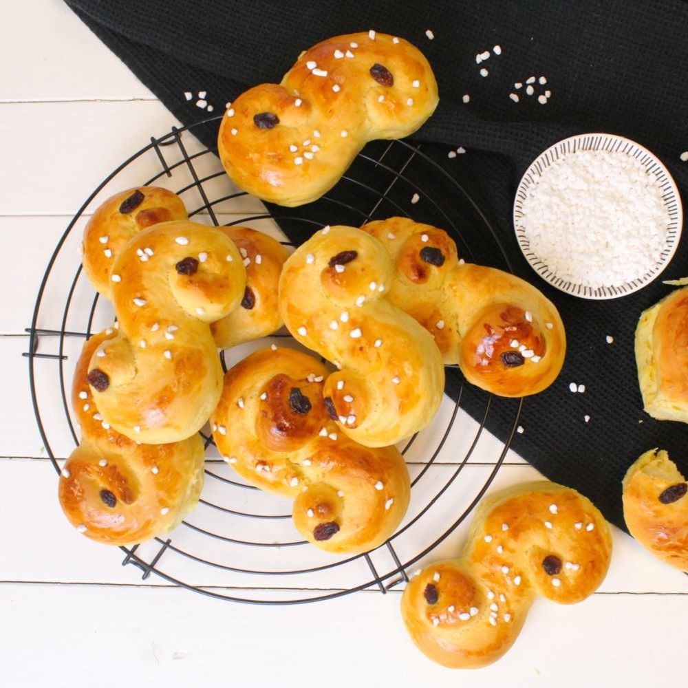 Gebäck auf einem Gitter. Goldbraune Brötchen mit Rosinen und Zuckerstreuseln. Auf schwarzem Hintergrund.