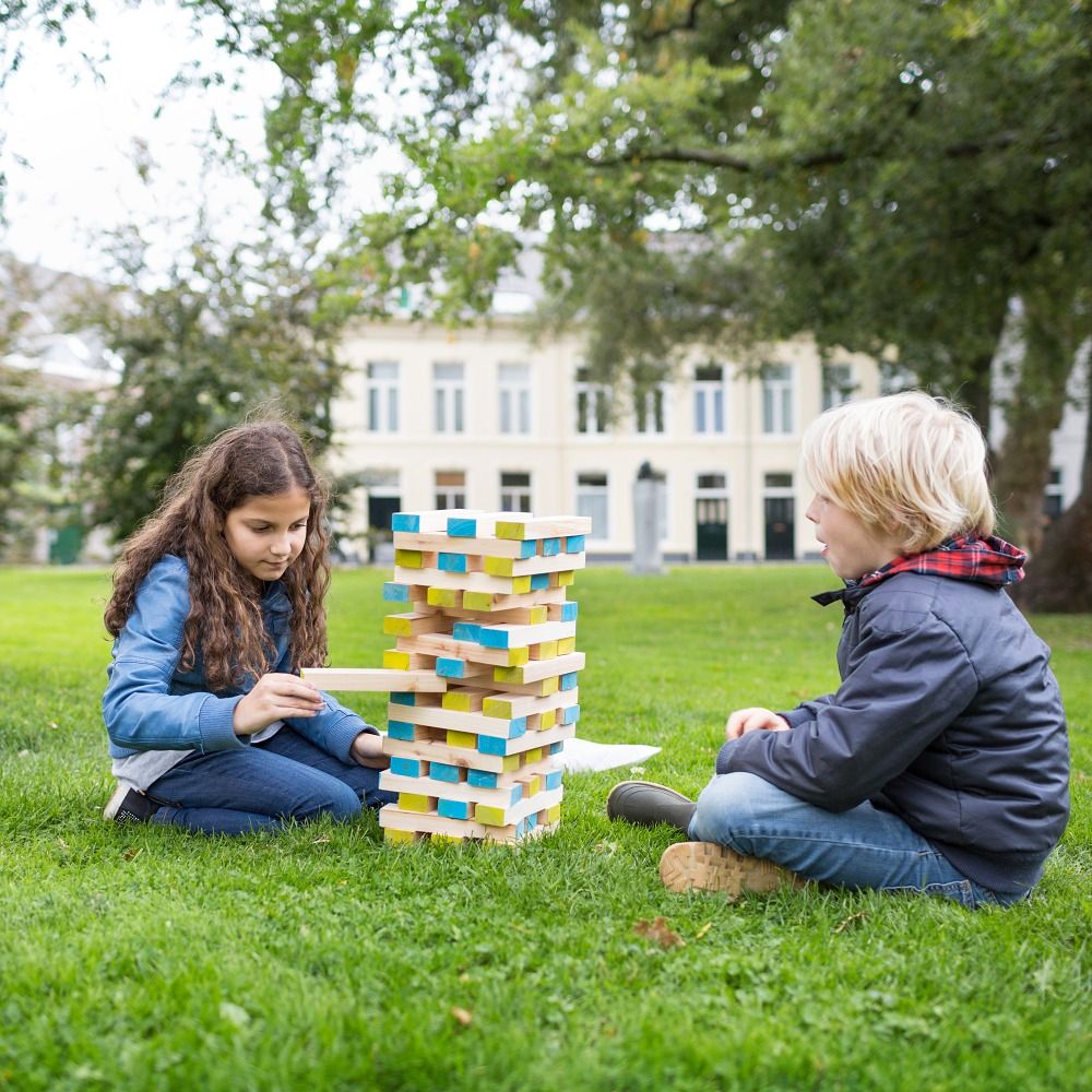 Zwei Kinder spielen im Freien mit einem Wackelturm. Ein Kind zieht einen Block heraus.