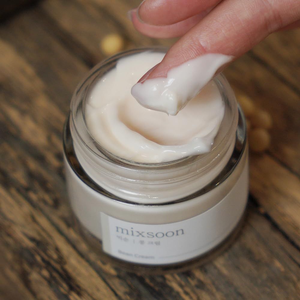 Glasbehälter mit Creme. Ein Finger berührt die Creme. Aufschrift: mixsoon Bean Cream. Hintergrund: Holz.