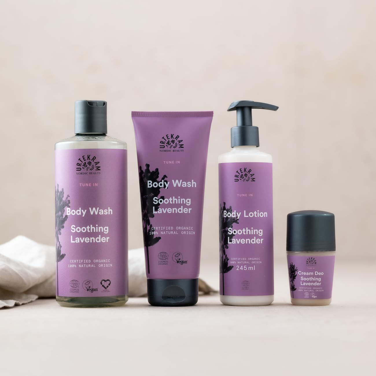 Vier Urtekram-Produkte: Body Wash, Body Lotion, Cream Deo, und ein weiteres Produkt. Lila Etiketten, schwarze Deckel. Bio-Zertifizierung.