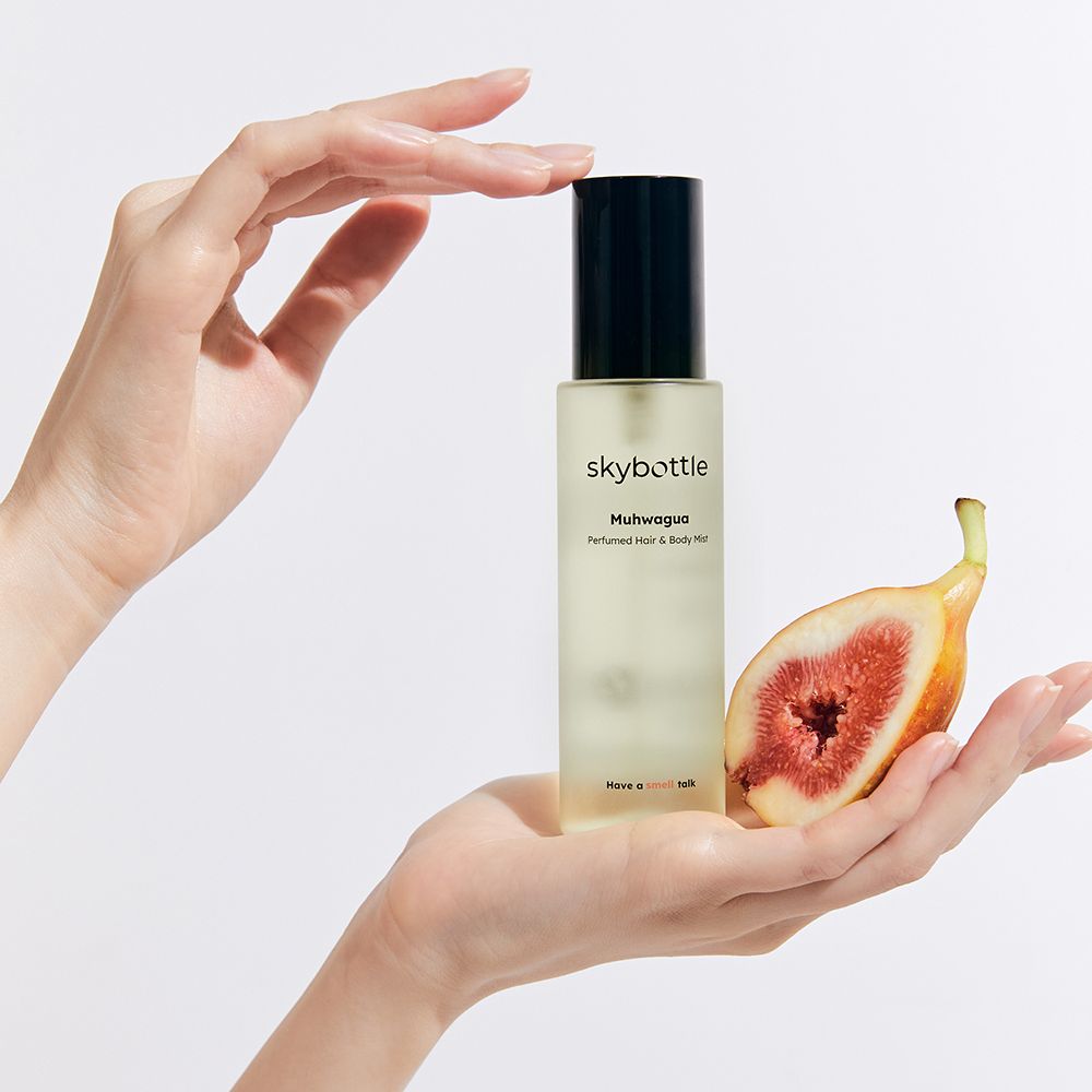 Hände halten Flakon und Feige. Flakon: skybottle, Muhwagua, Perfumed Hair & Body Mist. Feige halbiert.