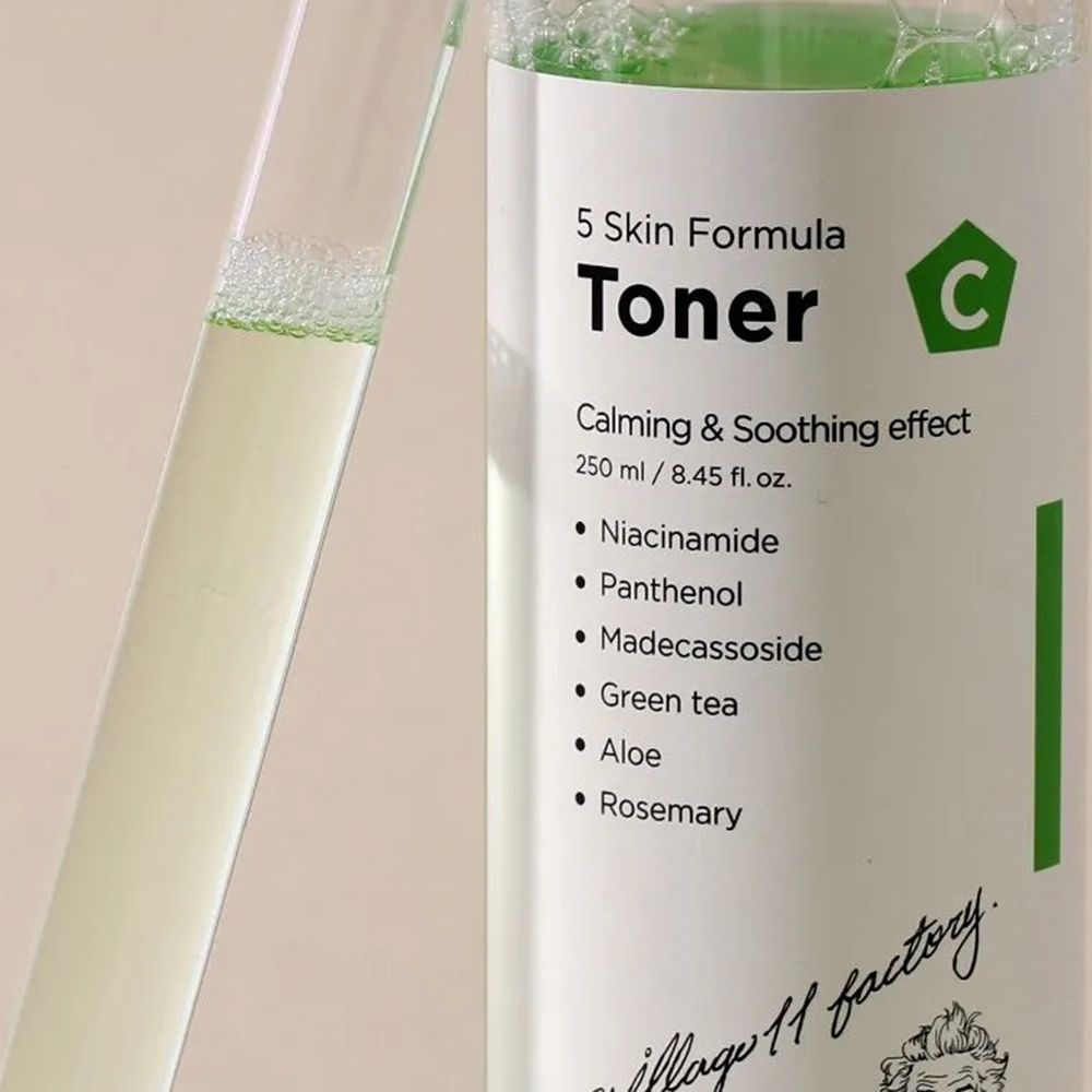 Nahaufnahme einer Flasche mit grünlicher Flüssigkeit. Text: Toner, Inhaltsstoffe. Marke: Village 11 Factory. Reagenzglas daneben.