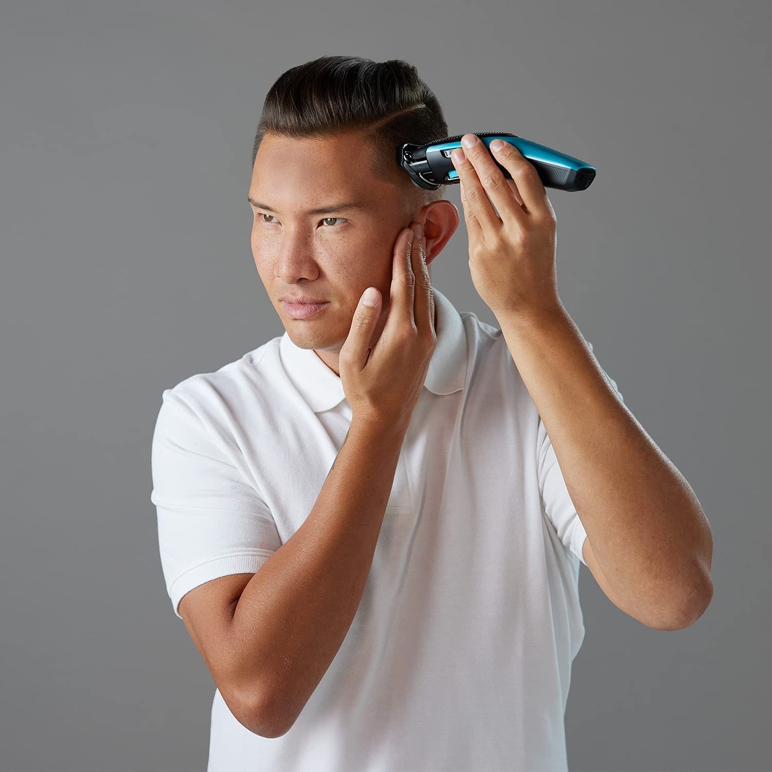 Mann schneidet Haare mit blau-schwarzem Haarschneider. Hält Hand an Kopf.