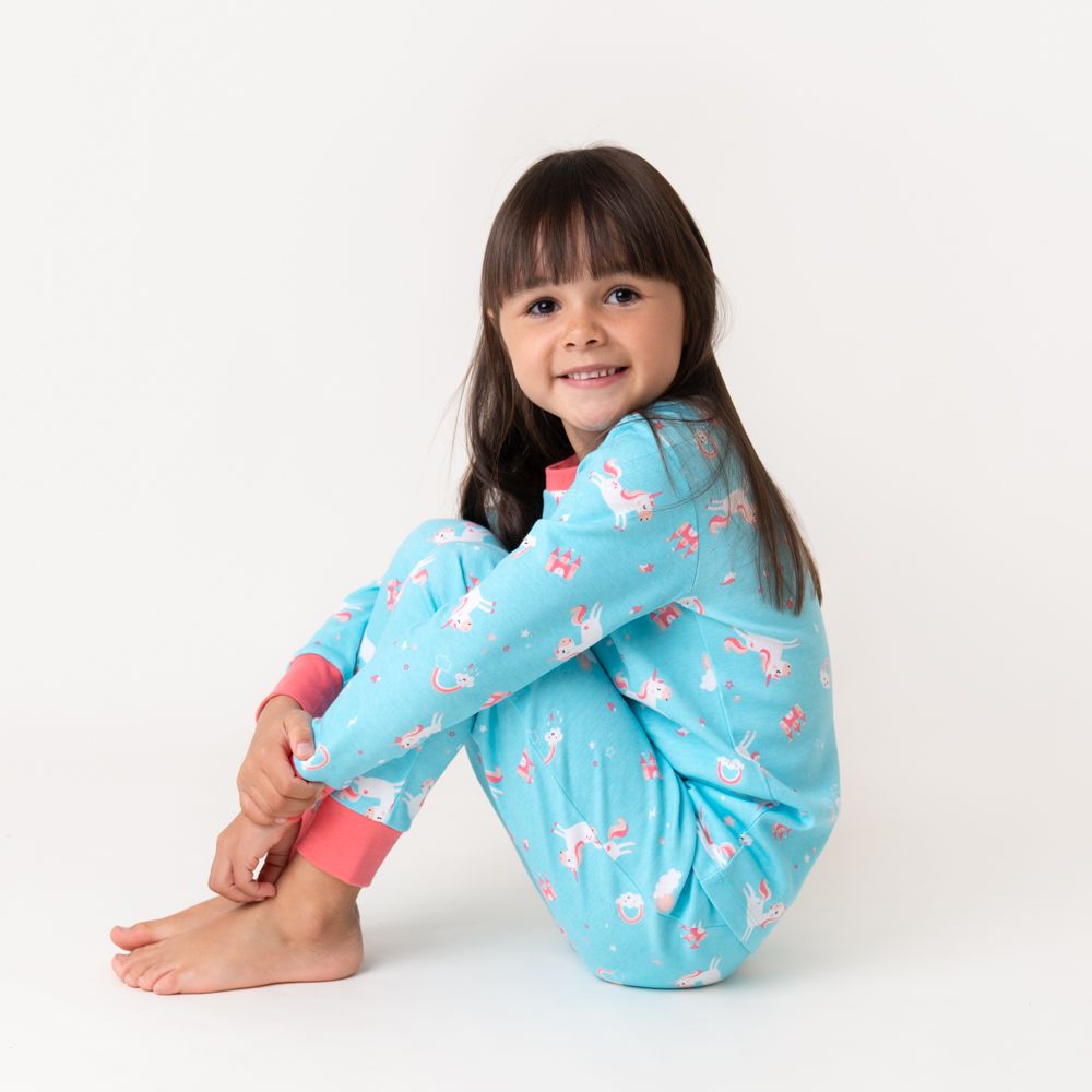 Kind trägt blauen Pyjama mit Einhorn-Muster. Rosa Bündchen. Kind sitzt auf dem Boden.