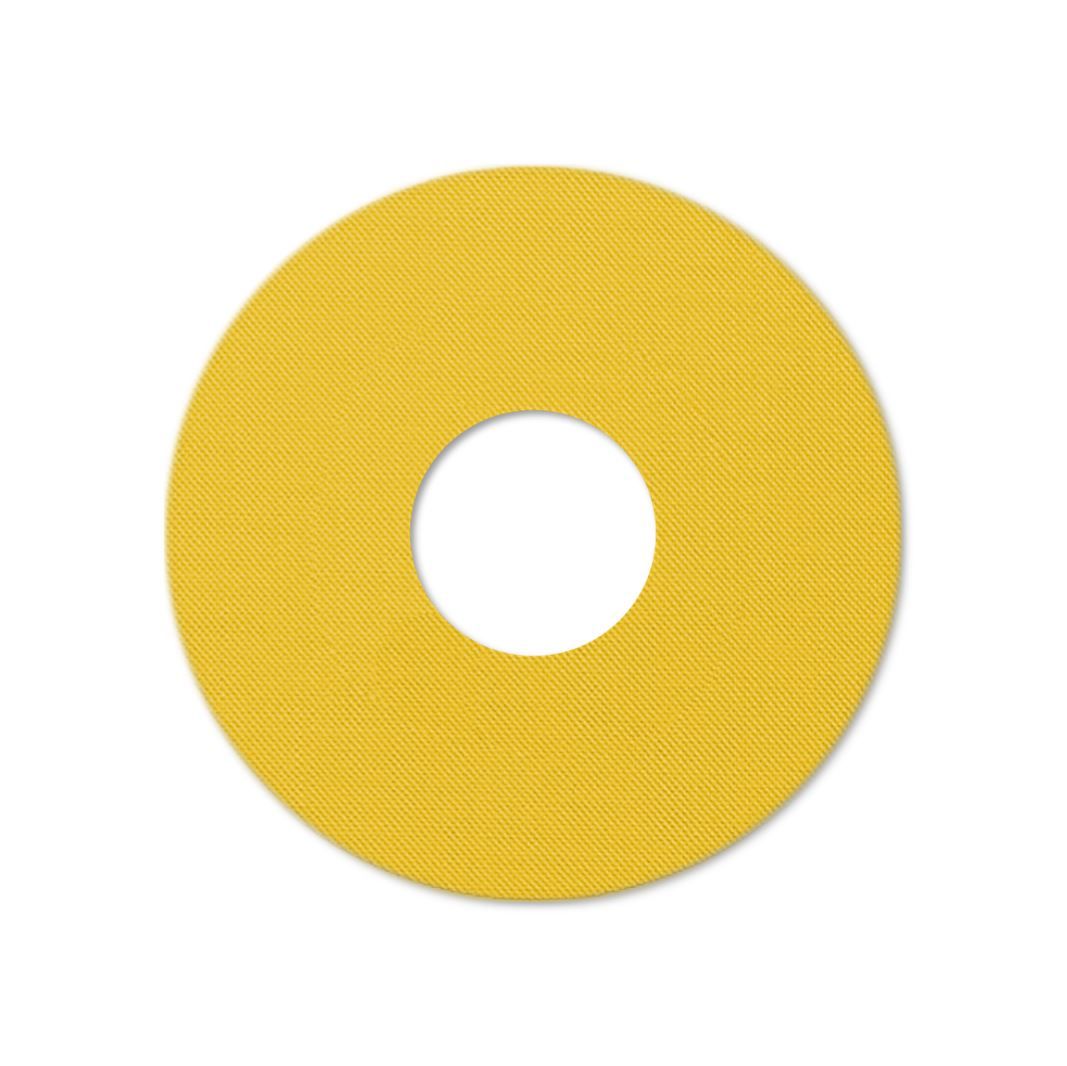 Gelber Katheterpatch mit zentralem Loch. Runde Form mit diagonaler Textur.