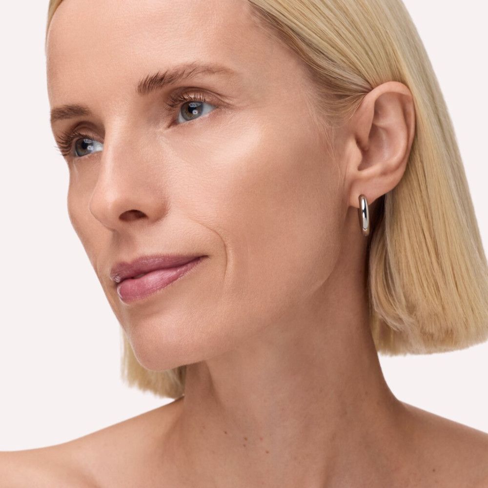 Porträt einer Frau mit blonden Haaren und silbernen Ohrringen. Haut wirkt ebenmäßig und glänzend.