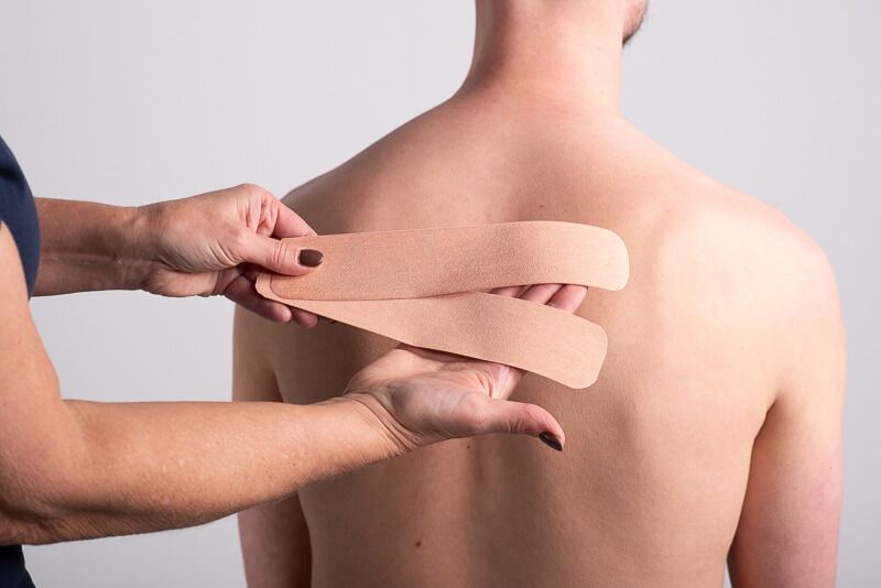 Person hält zwei beige Kinesiotape-Streifen vor dem Rücken einer anderen Person.