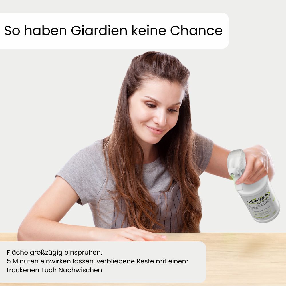 Frau sprüht mit ViPiBaX Giardien EX® Spray auf eine Holzoberfläche. Text: Großzügig einsprühen, 5 Minuten einwirken lassen, trocken wischen.