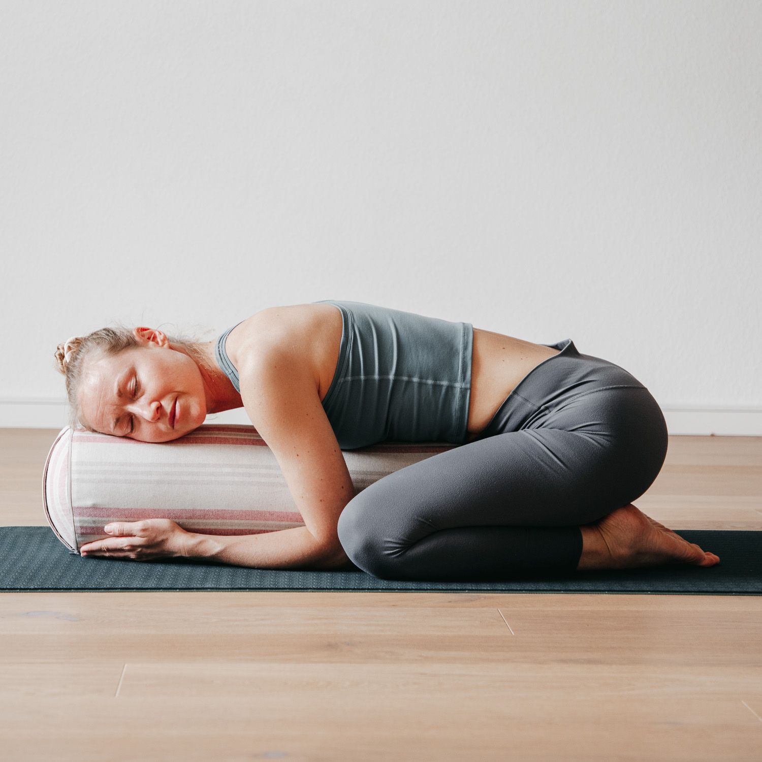 Frau in Yoga-Pose, Kopf auf einem Yoga-Bolster mit Streifenmuster. Auf Yogamatte.