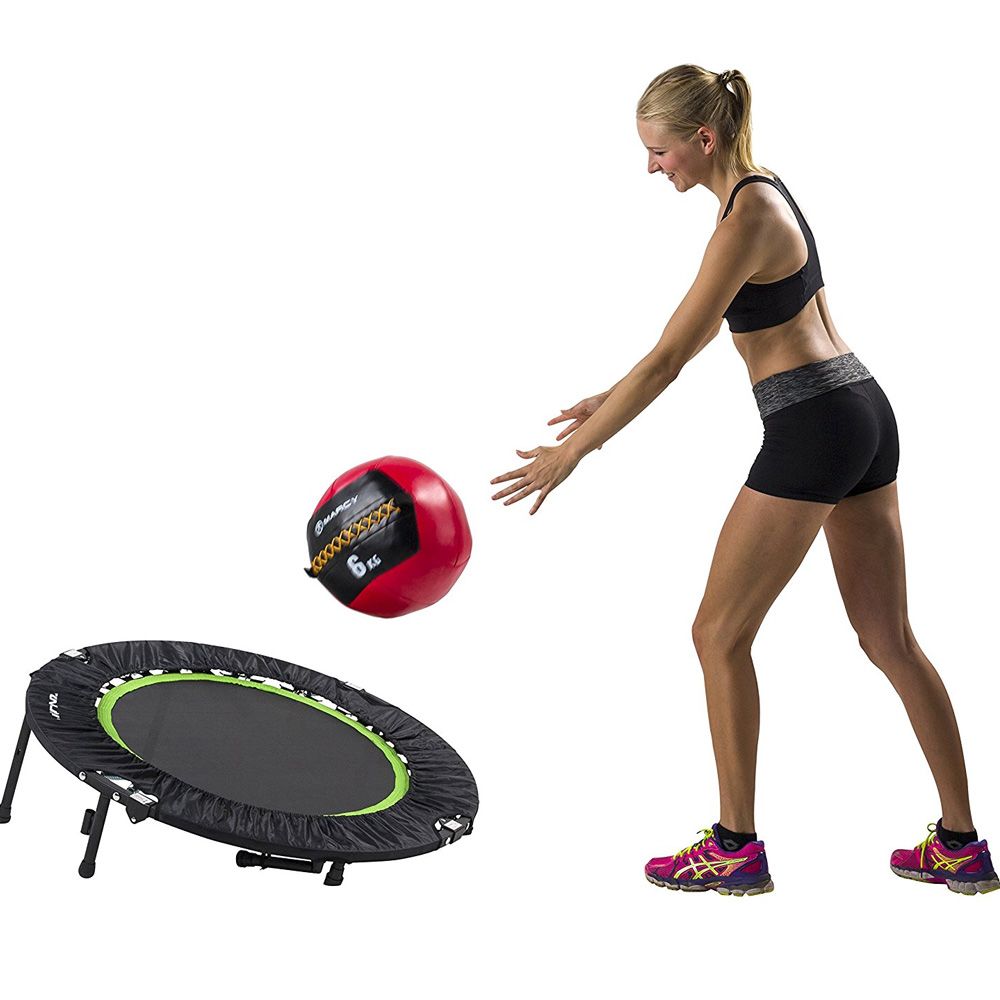 Frau wirft Medizinball neben Fitness Trampolin. Trampolin mit Haltebügel, schwarzer Bezug.
