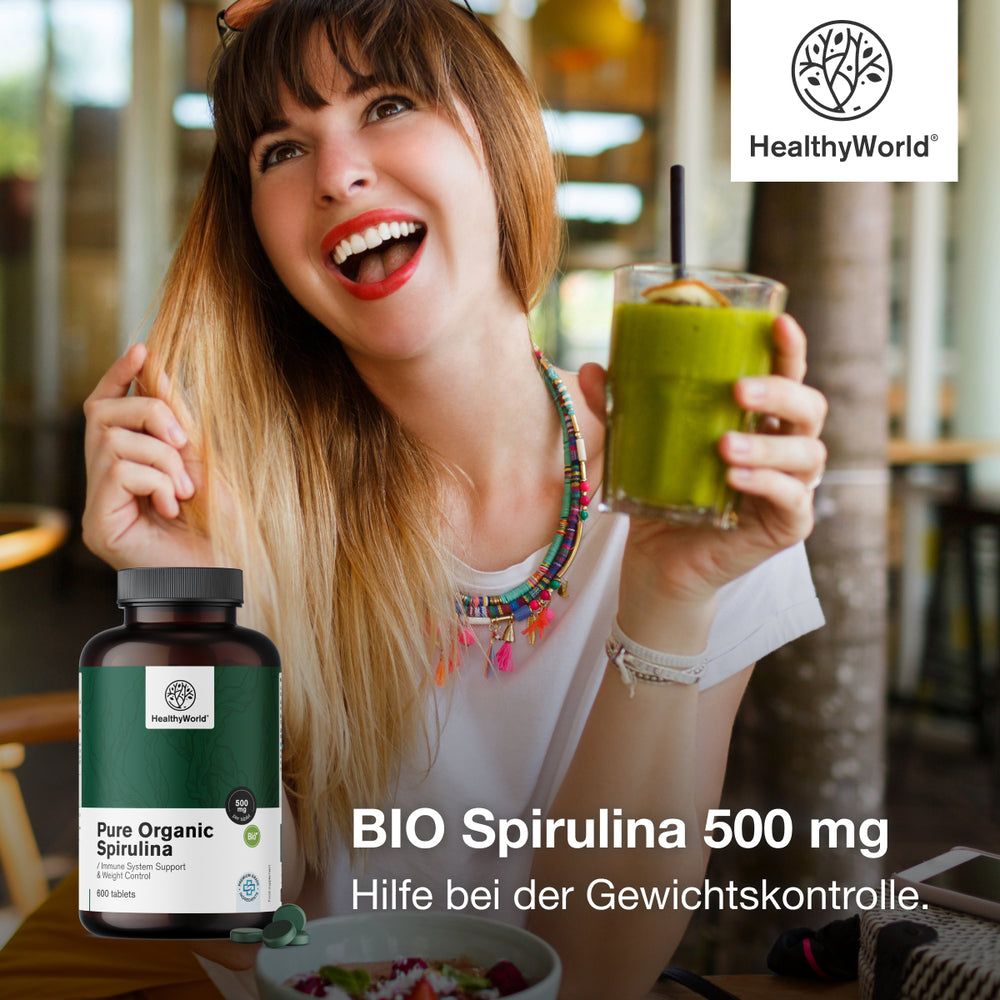Frau hält ein Glas Smoothie und eine Flasche. Aufschrift: BIO Spirulina 500 mg. Flasche mit grünem Etikett. Logo: HealthyWorld.