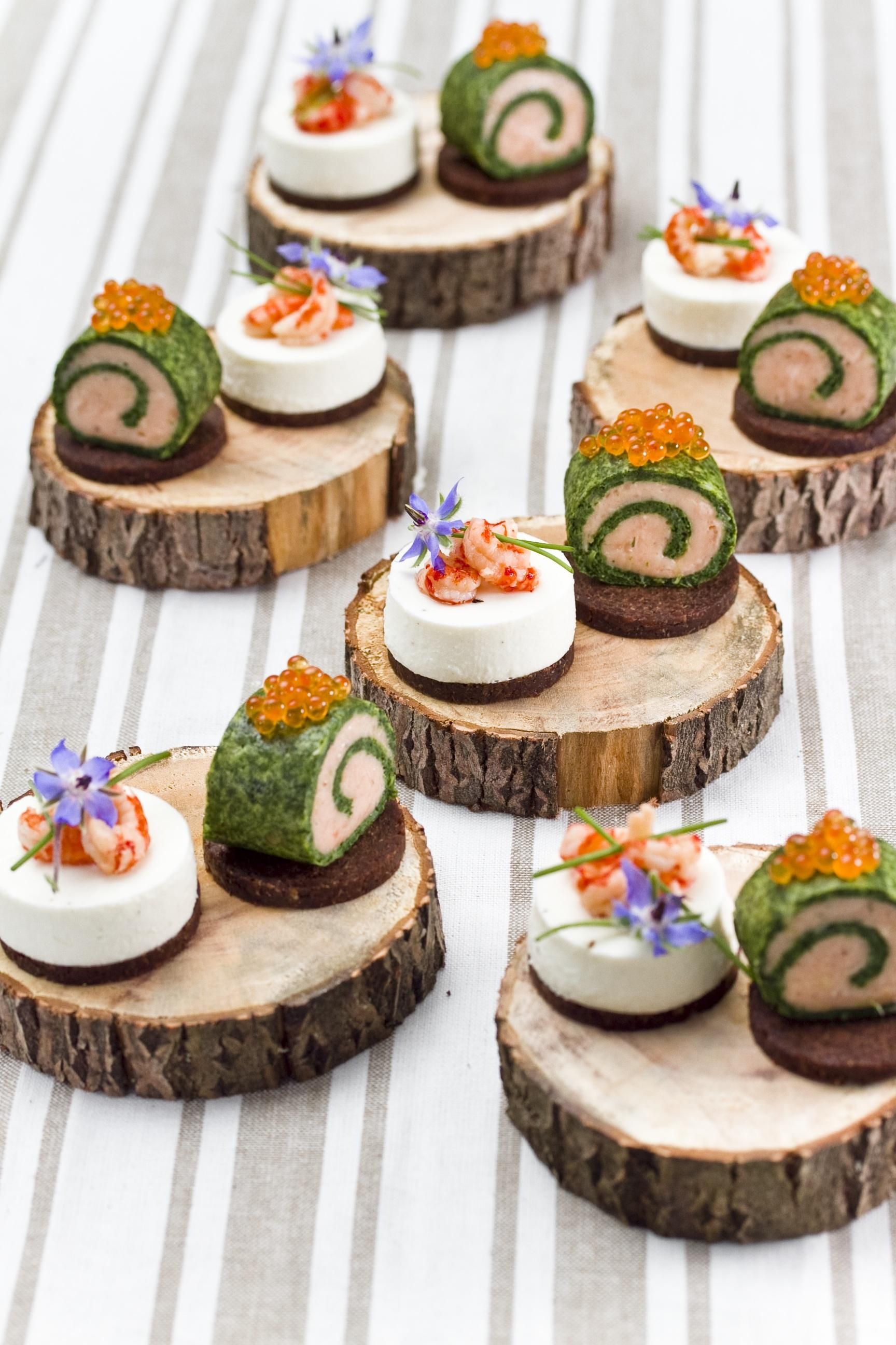 Holzscheiben mit Tapas. Auf Cracker-Basis, mit Creme, Lachs, Kaviar und Blüten dekoriert.