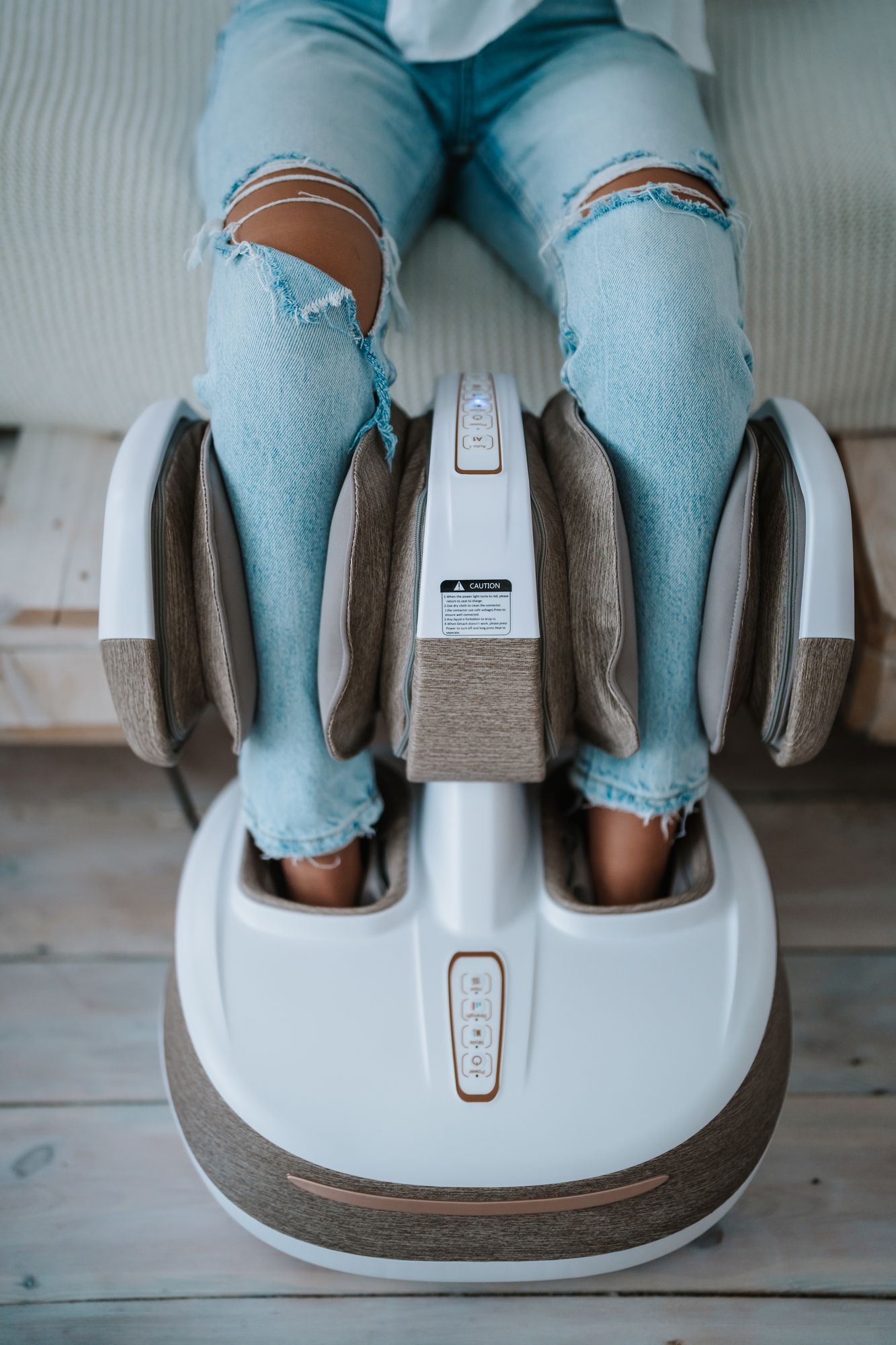 Draufsicht auf ein weißes Massagegerät, in dem sich Füße befinden. Die Person trägt Jeans. Bedienfeld sichtbar.