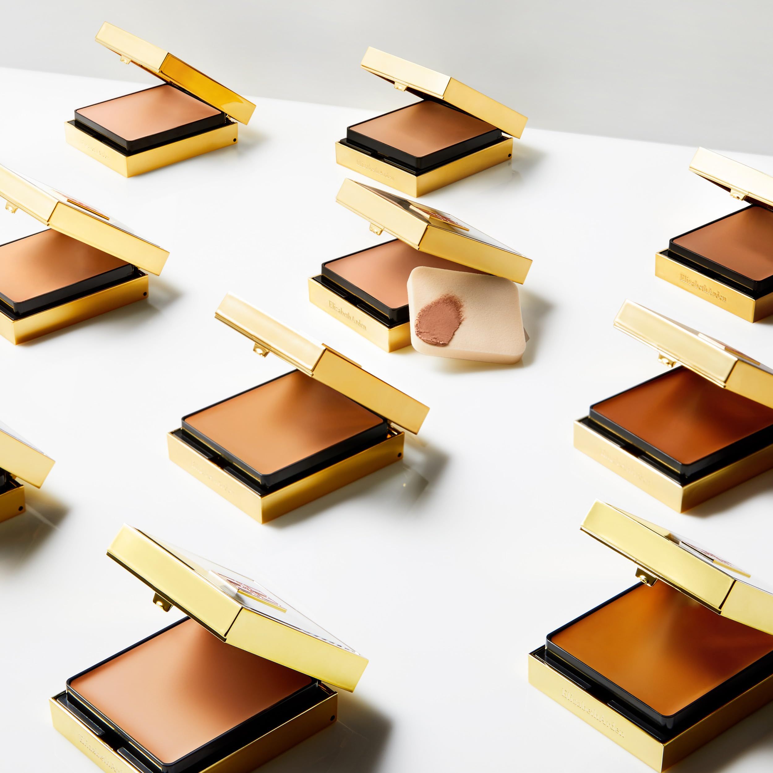 Mehrere goldfarbene Make-up-Kompaktverpackungen mit Spiegel und Schwamm. Deckel geöffnet.