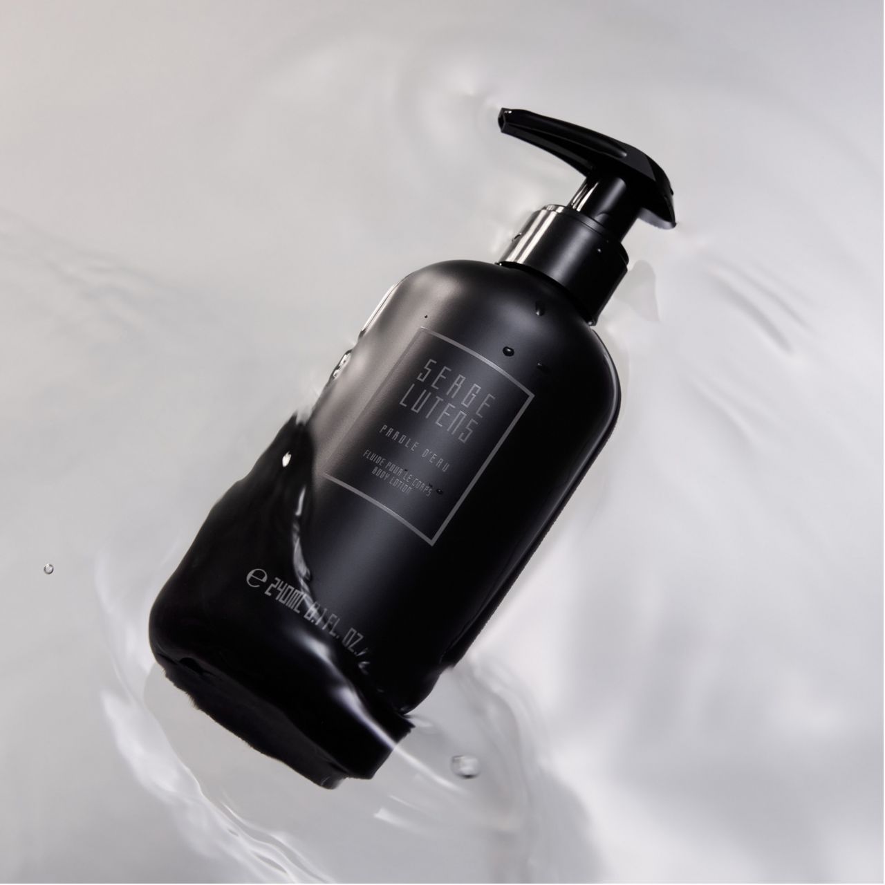 Schwarze Flasche mit Pumpe im Wasser. Etikett mit Schriftzug. Unten steht "e 240ml 8.1 fl. oz.".